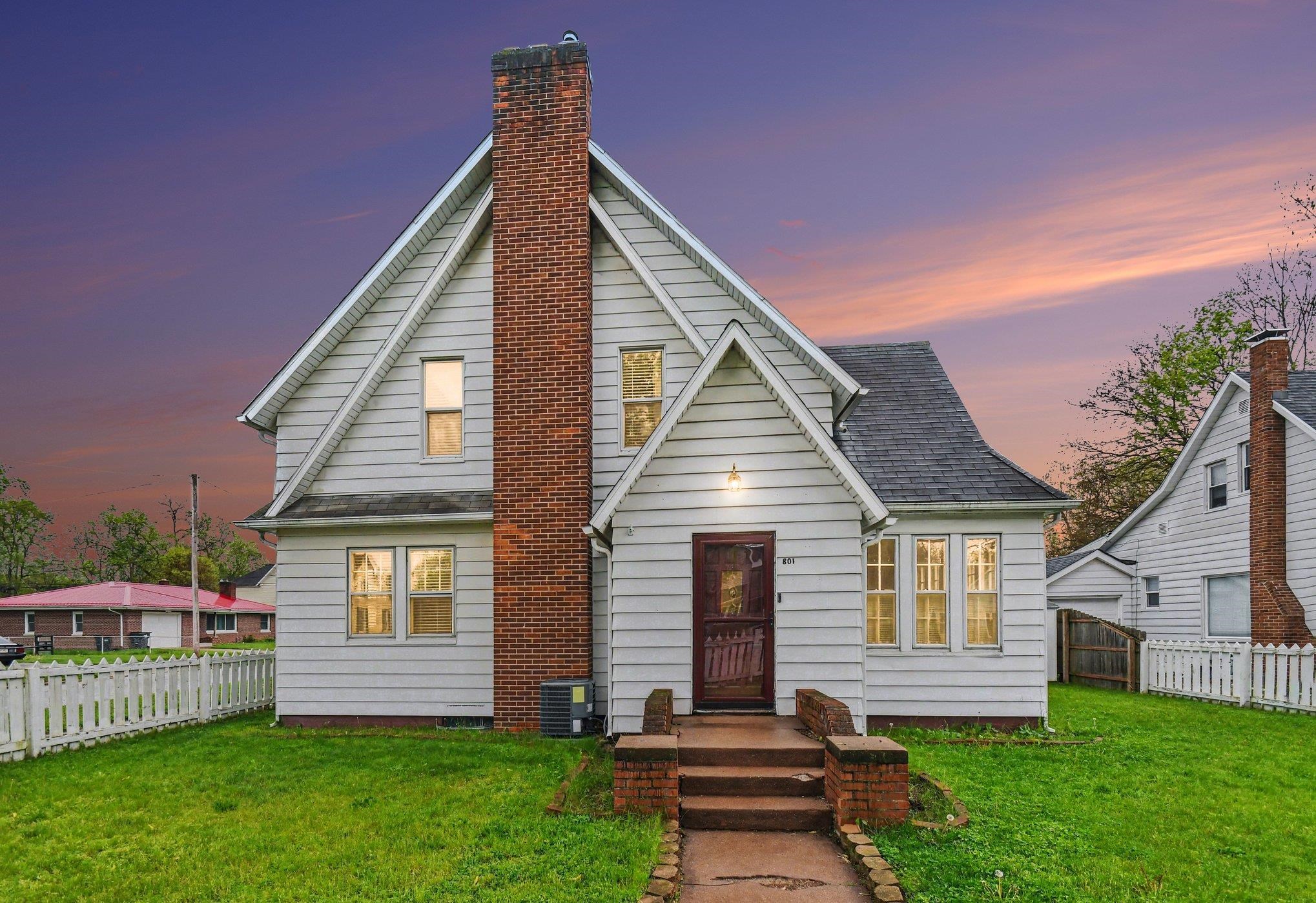 Gabled facade home featuring white siding and a prominent brick chimney