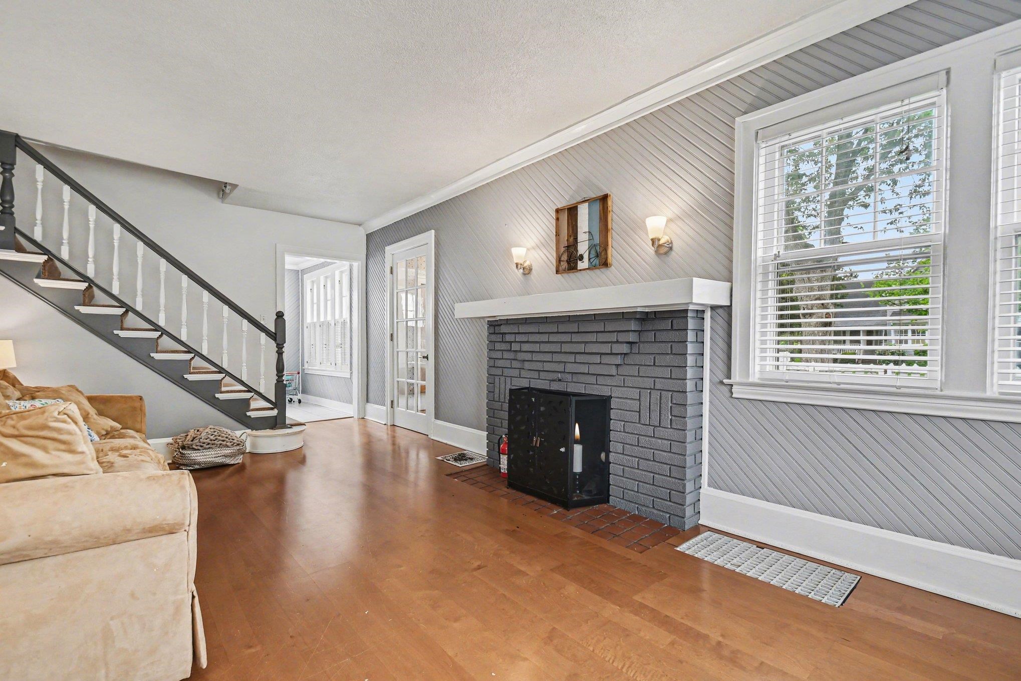 Living area featuring wood-finish flooring, a painted brick fireplace with a white mantel, and diagonal wood paneling on the accent wall