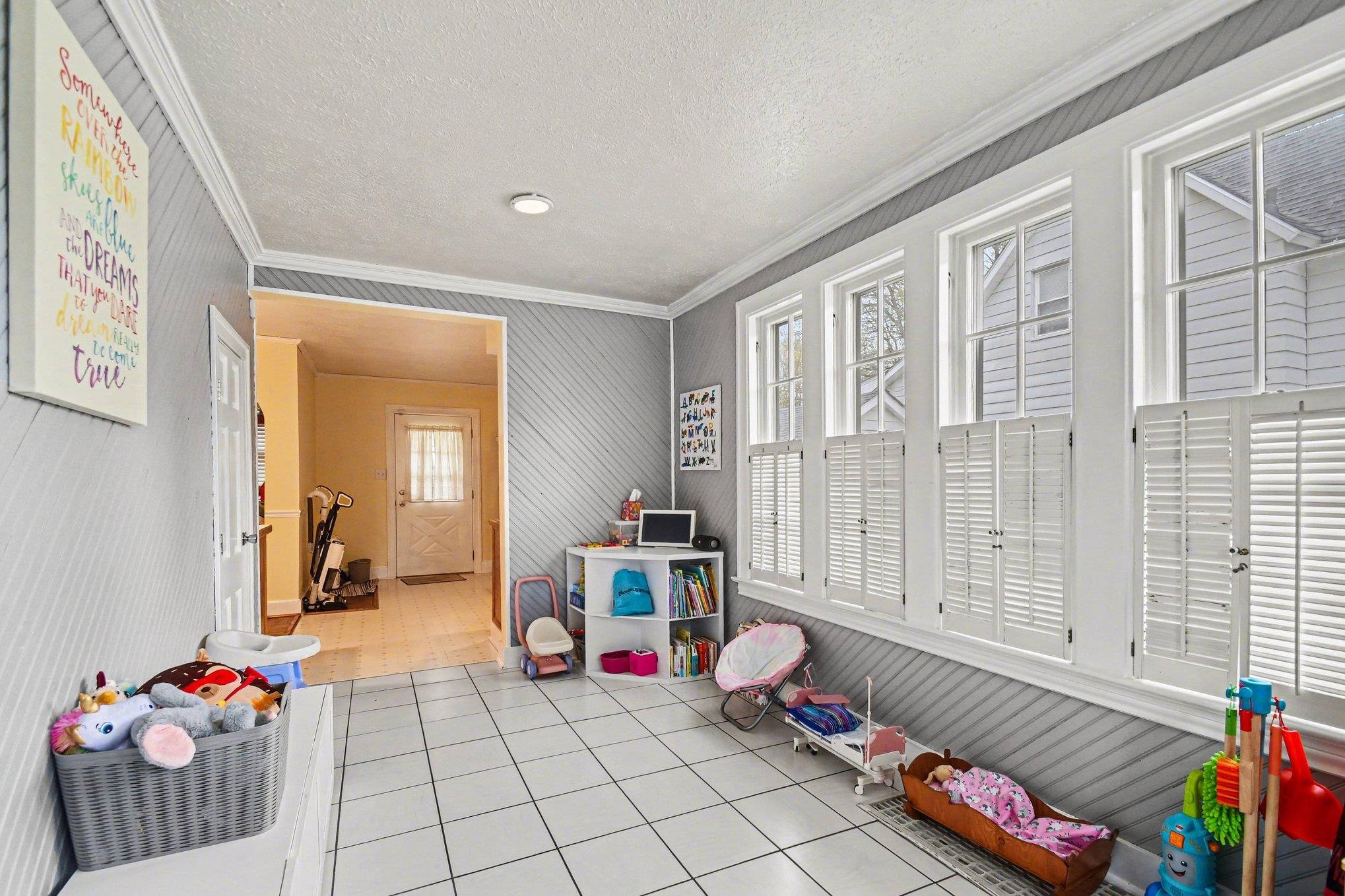 Room with white square tile flooring, diagonal wall paneling, and a series of four multi-pane windows with white plantation shutters