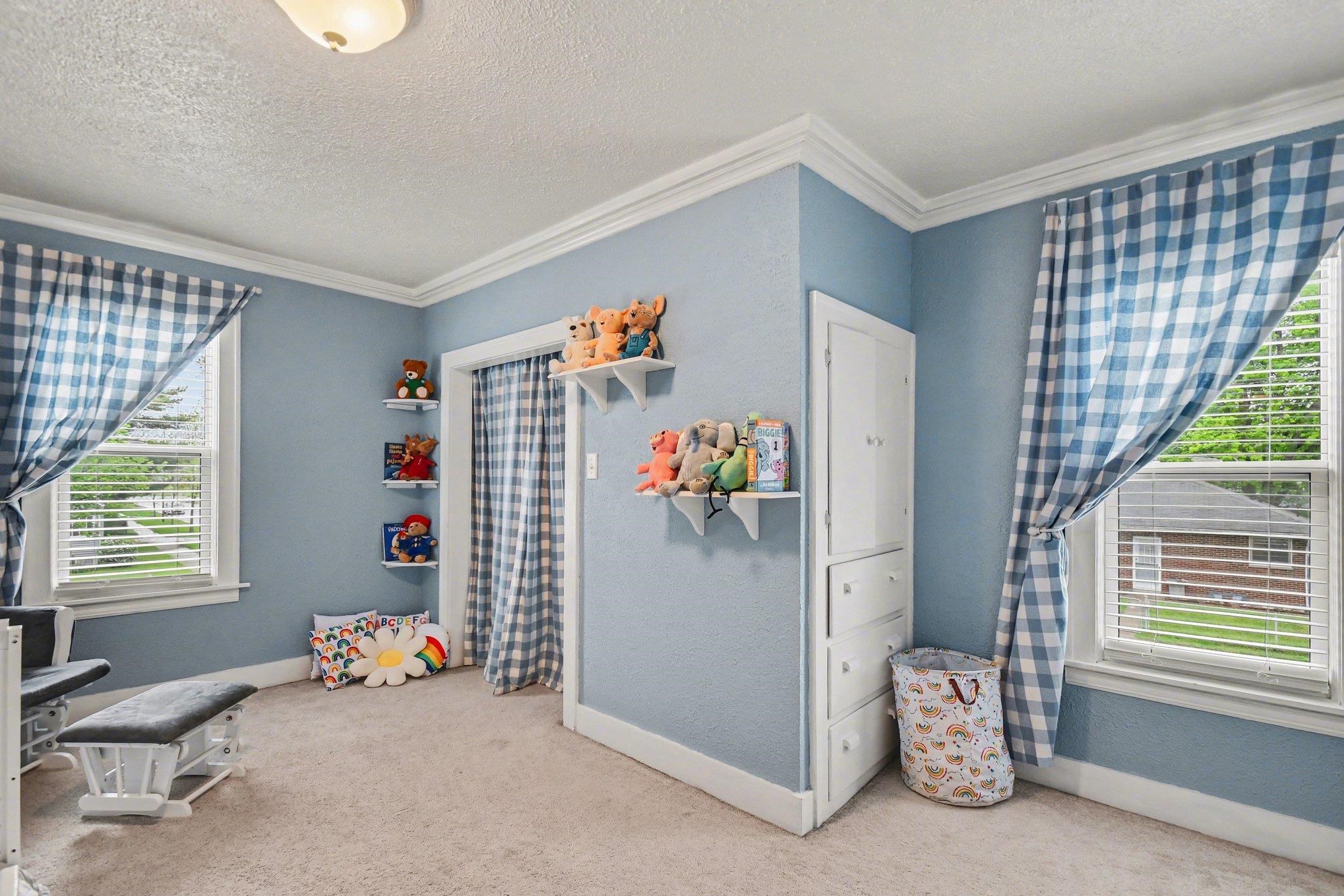 Room featuring light blue walls, two large windows with blinds, built-in shelving, carpet flooring, and white trim