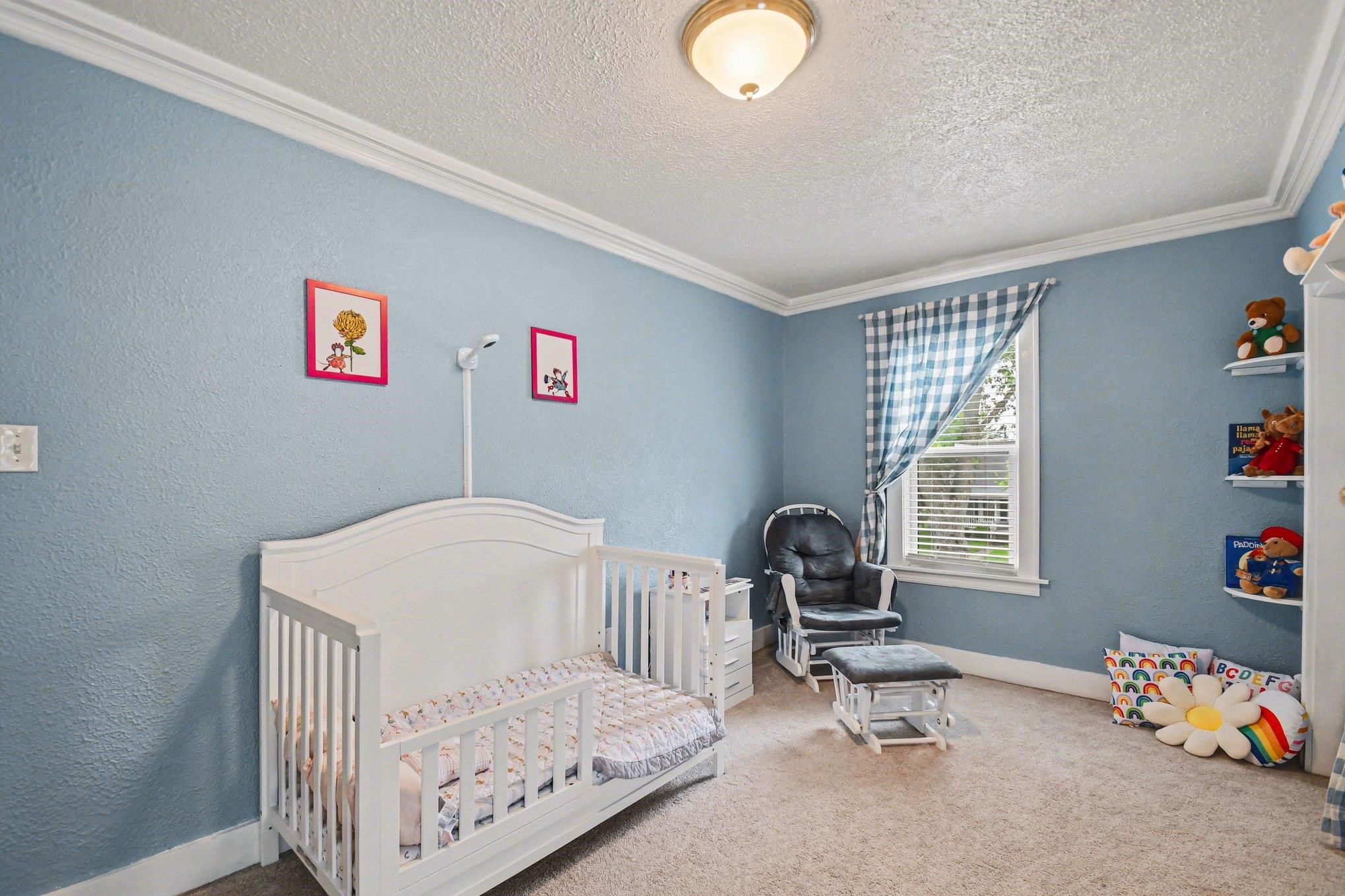 Carpeted room featuring a single window with blinds, light blue walls, white crown molding, and built-in shelving