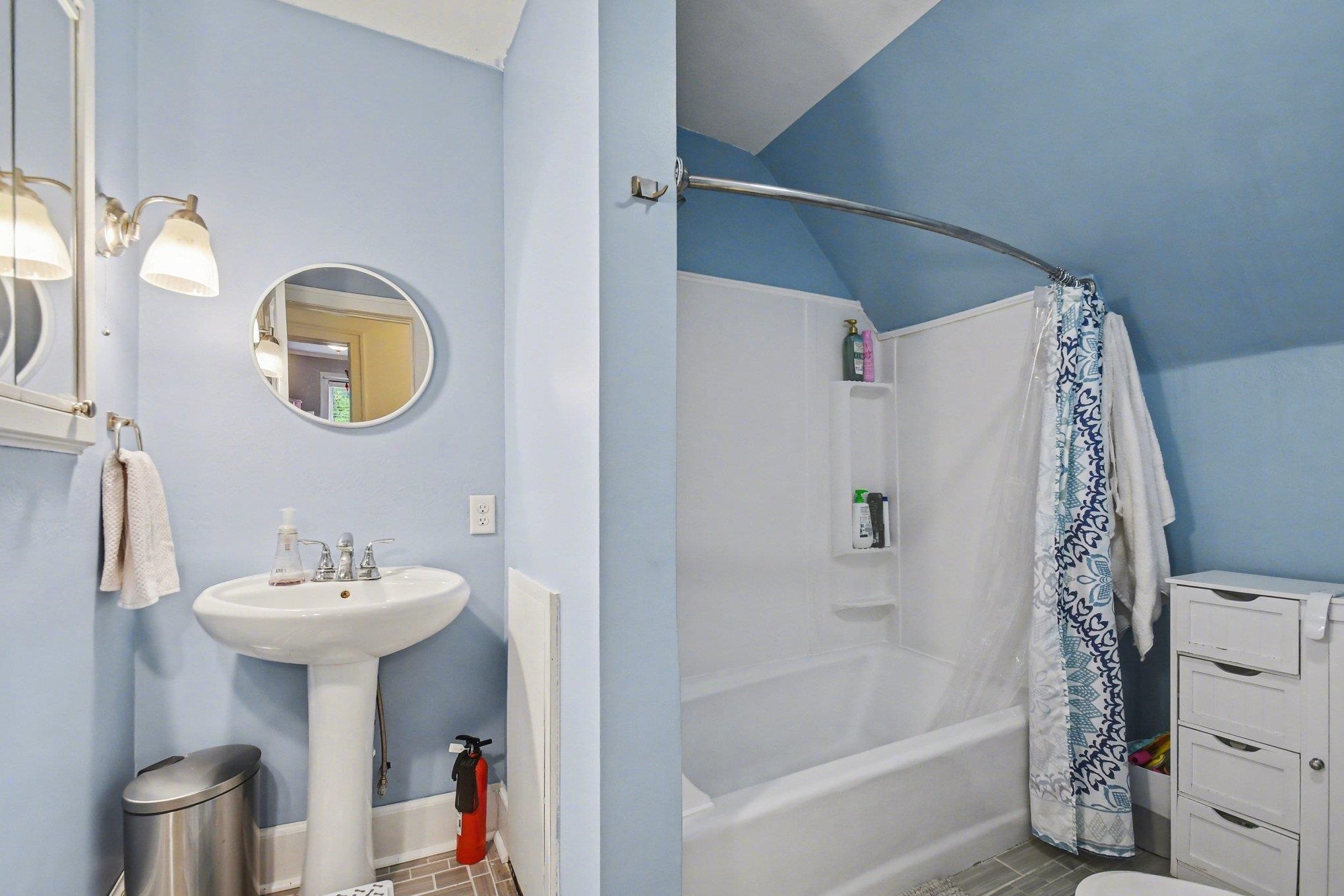 Bathroom featuring a pedestal sink, wall-mounted light fixture, and a white tub with a shower surround