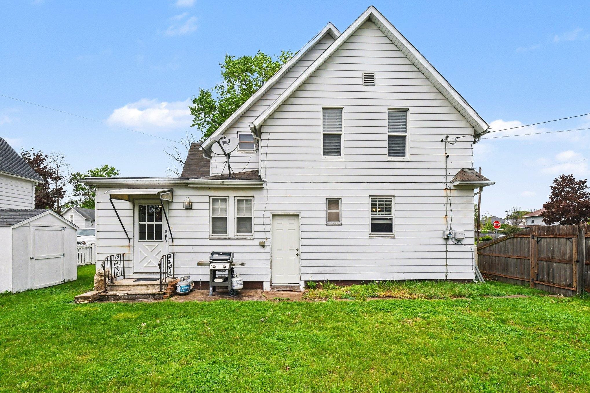 Rear exterior featuring white horizontal siding, a gabled roofline, a rear entry door with storm awning, and an additional white exterior door