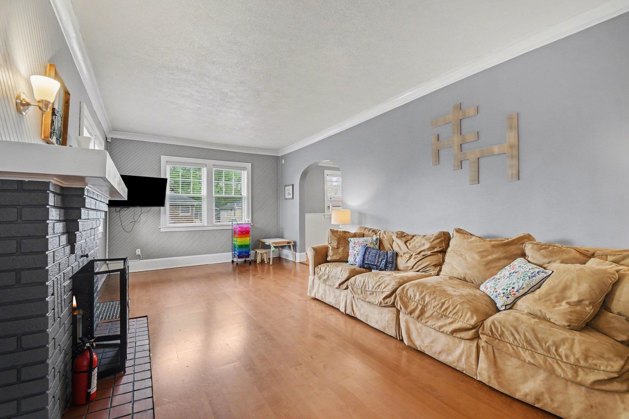 Living area featuring wood-finish flooring, a painted brick fireplace with a white mantel, and a window with white trim