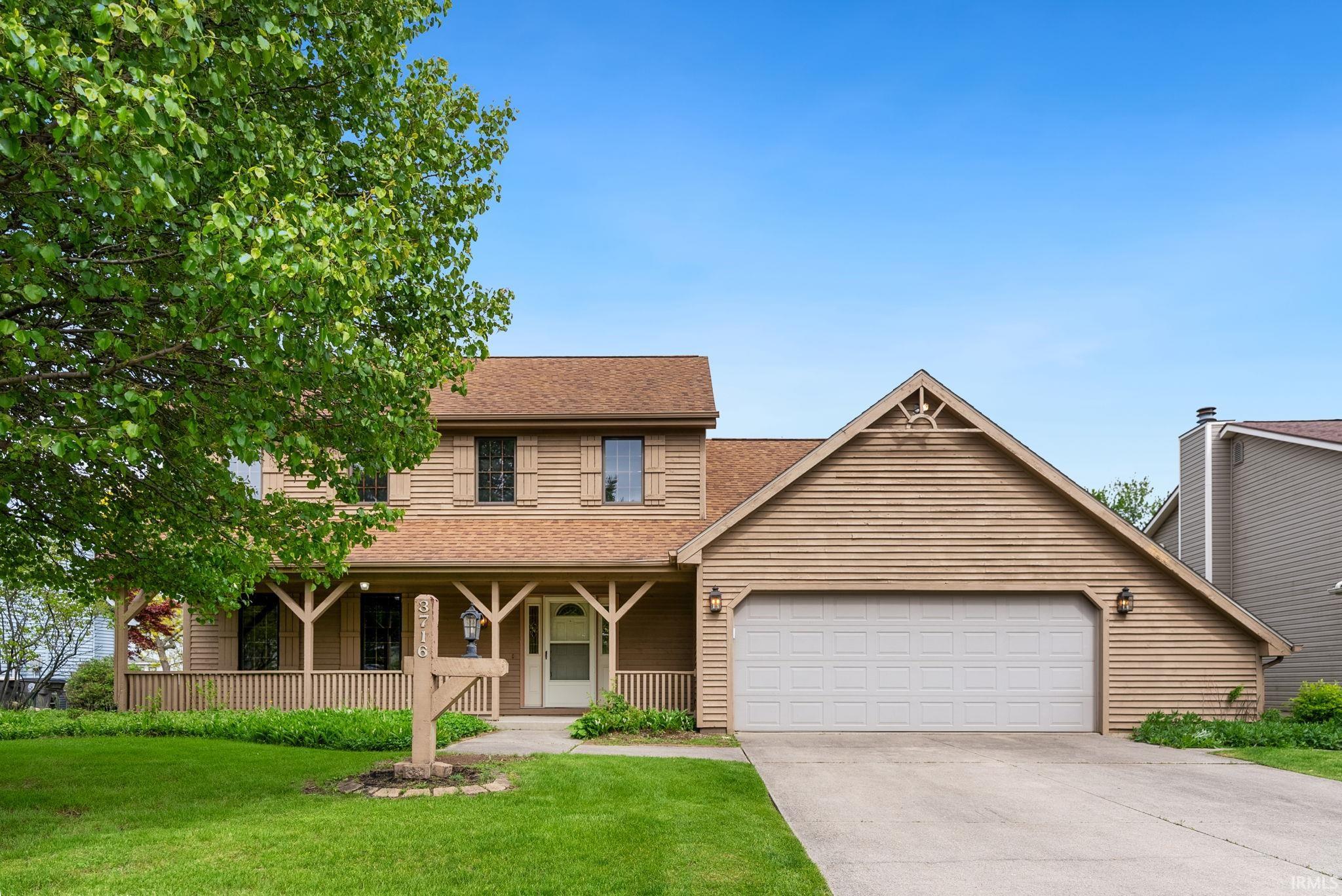 Two-story residence featuring light brown siding, a covered front porch, and a two-car garage