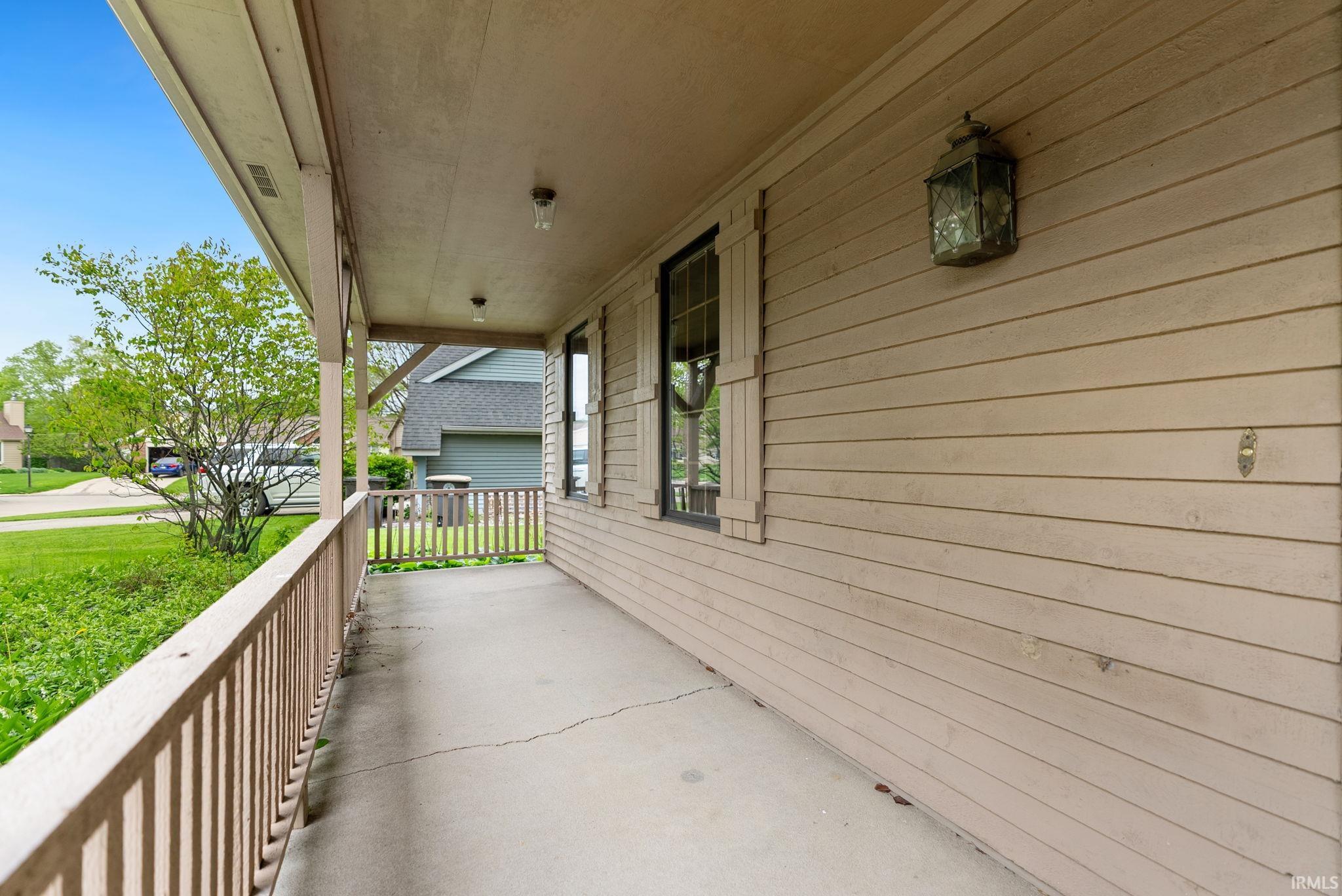 Covered front porch featuring a wood railing and concrete flooring