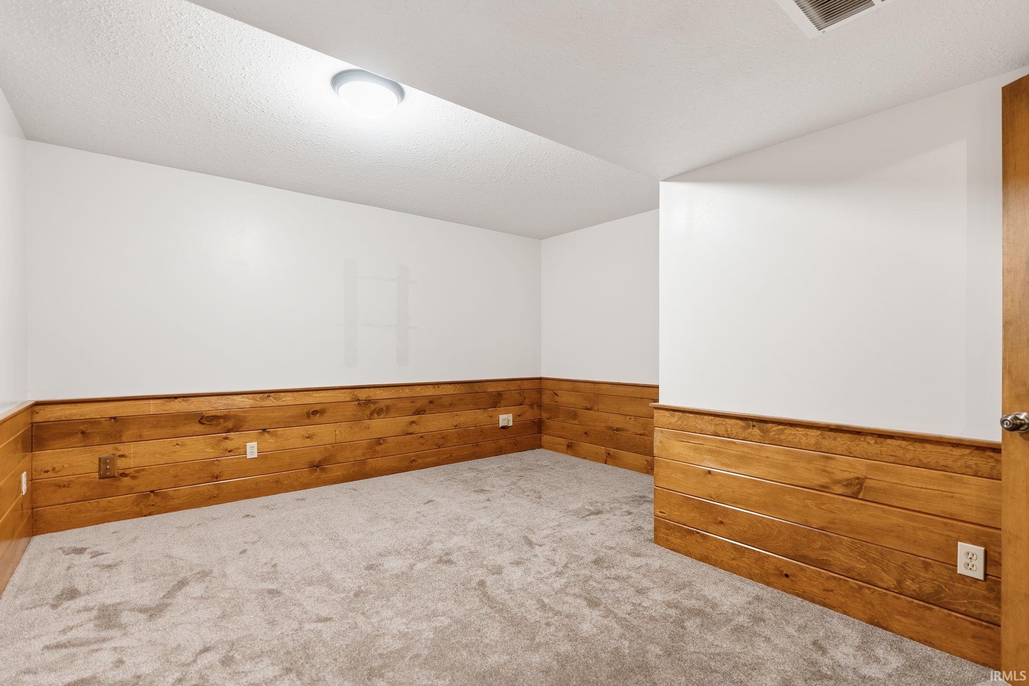 Room featuring wood paneling, white walls, and light-colored carpeting