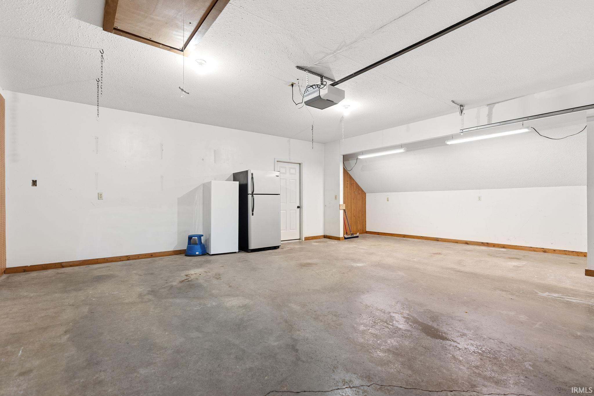 Spacious garage featuring a concrete floor, white painted walls, wood trim, and bright overhead lighting