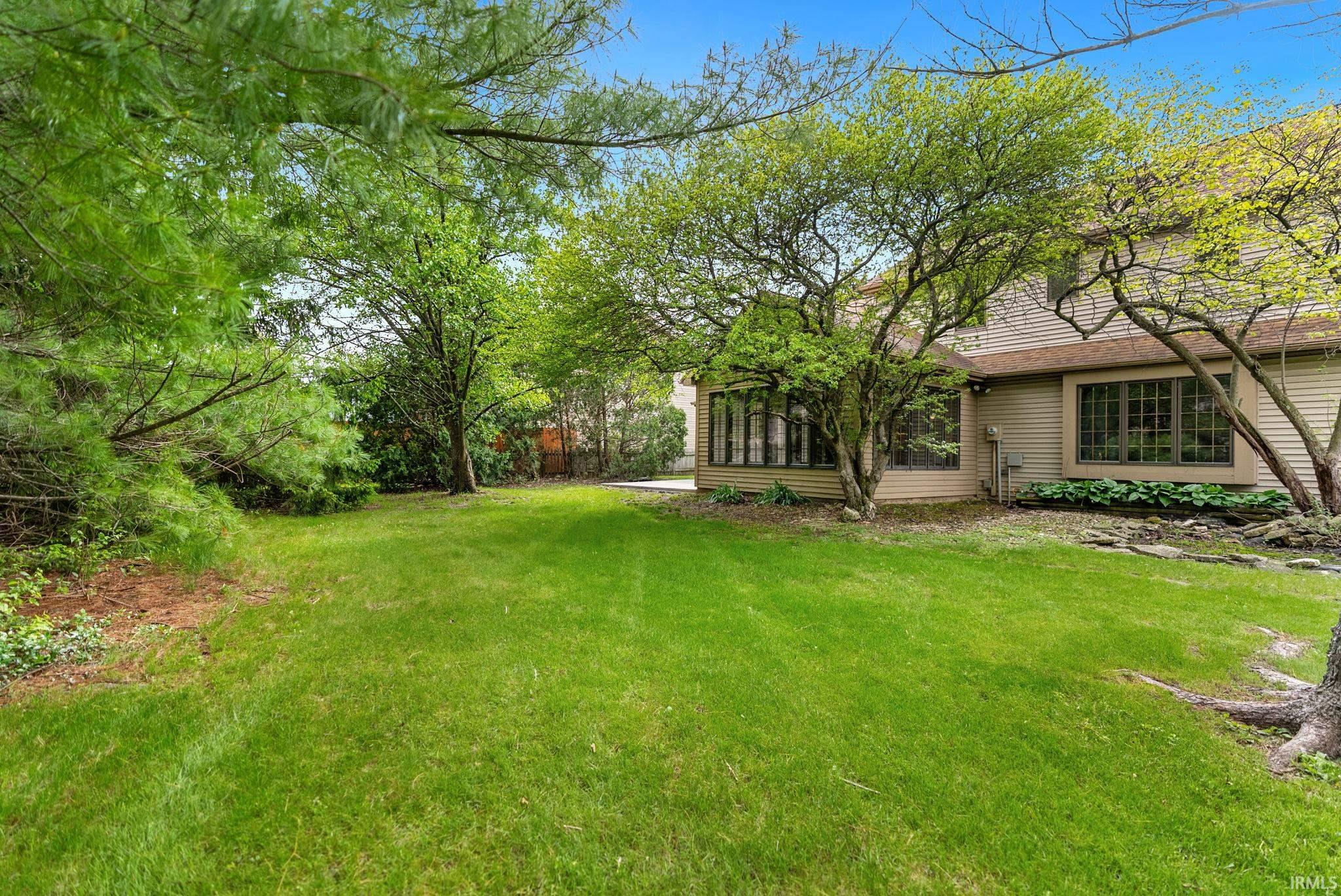 Expansive green lawn with mature trees and a two-story home featuring bay windows and an additional window bank