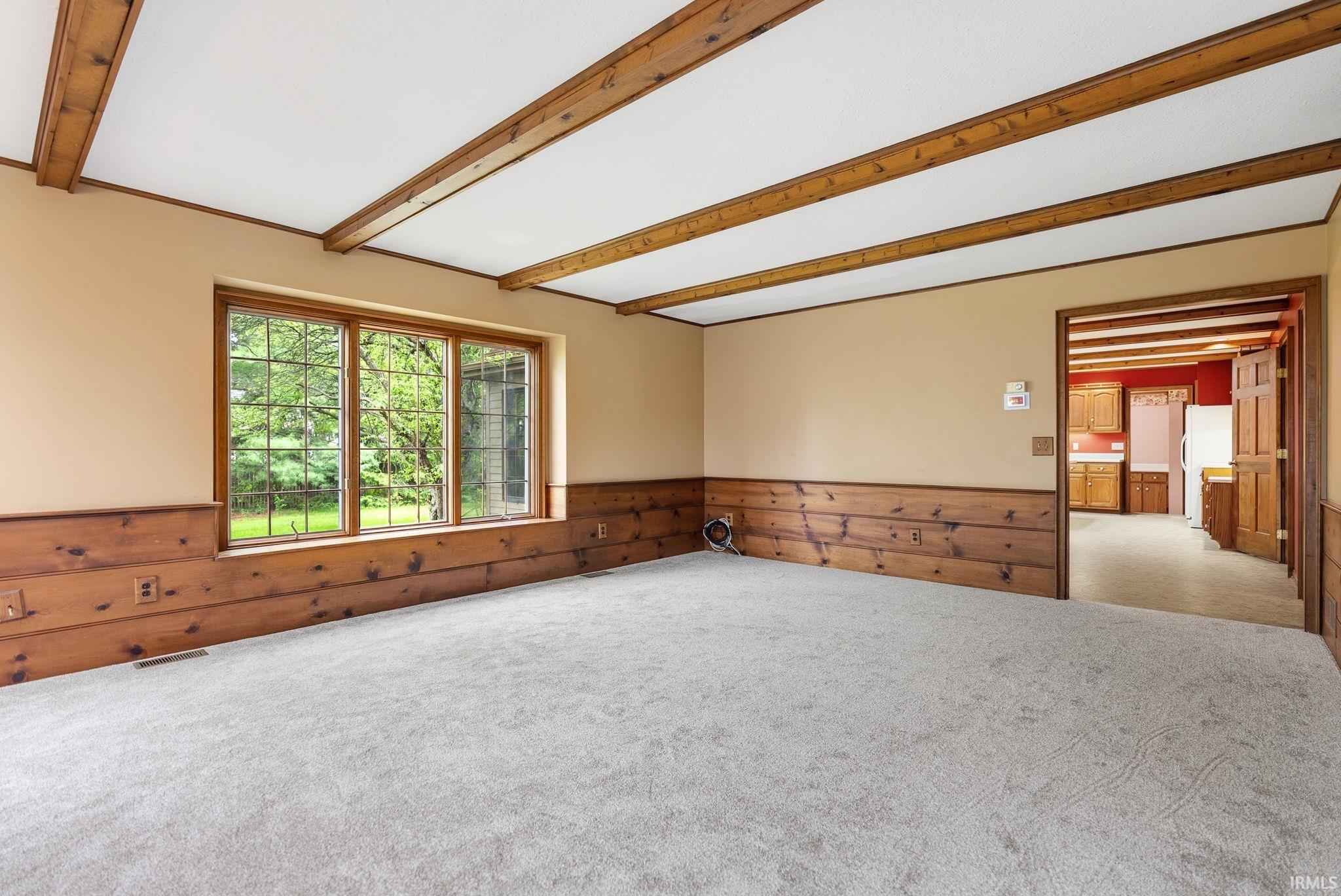 Windowed living space featuring exposed wood ceiling beams and wood-paneled wainscoting