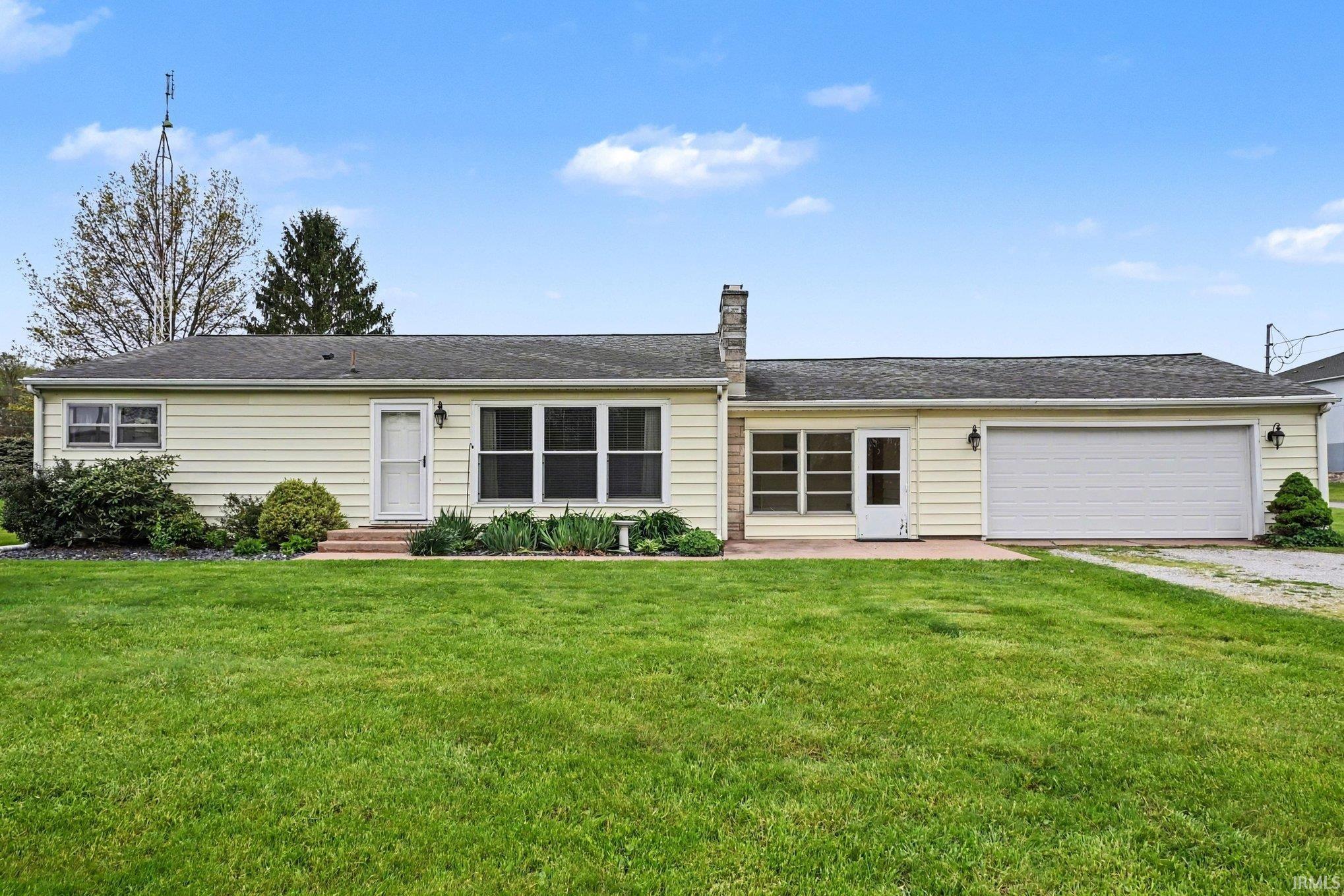 Ranch-style residence featuring light-colored siding, a stone chimney, and a front lawn