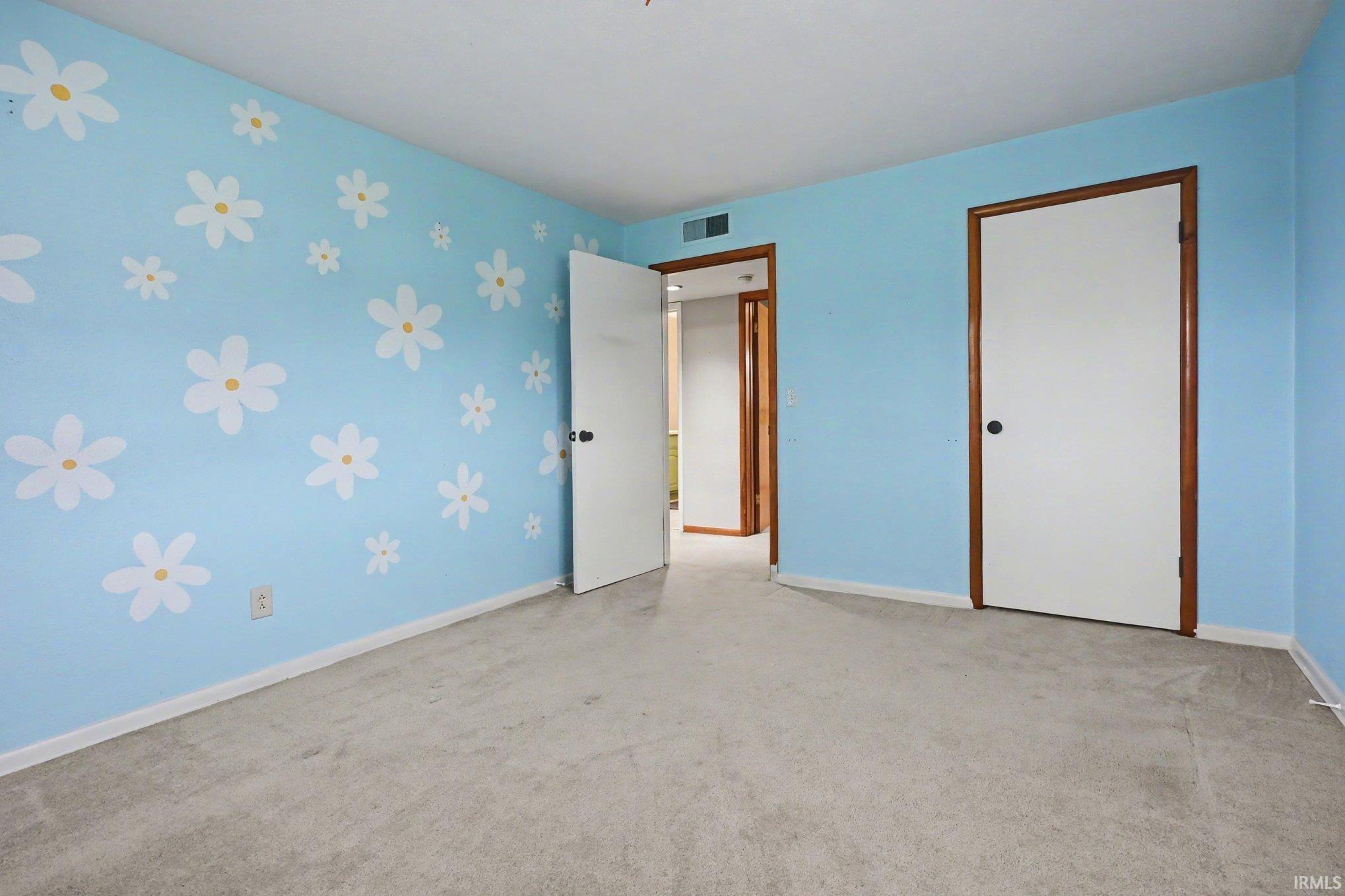 Room featuring light blue walls with white floral accents, neutral-toned carpet flooring, and white trim