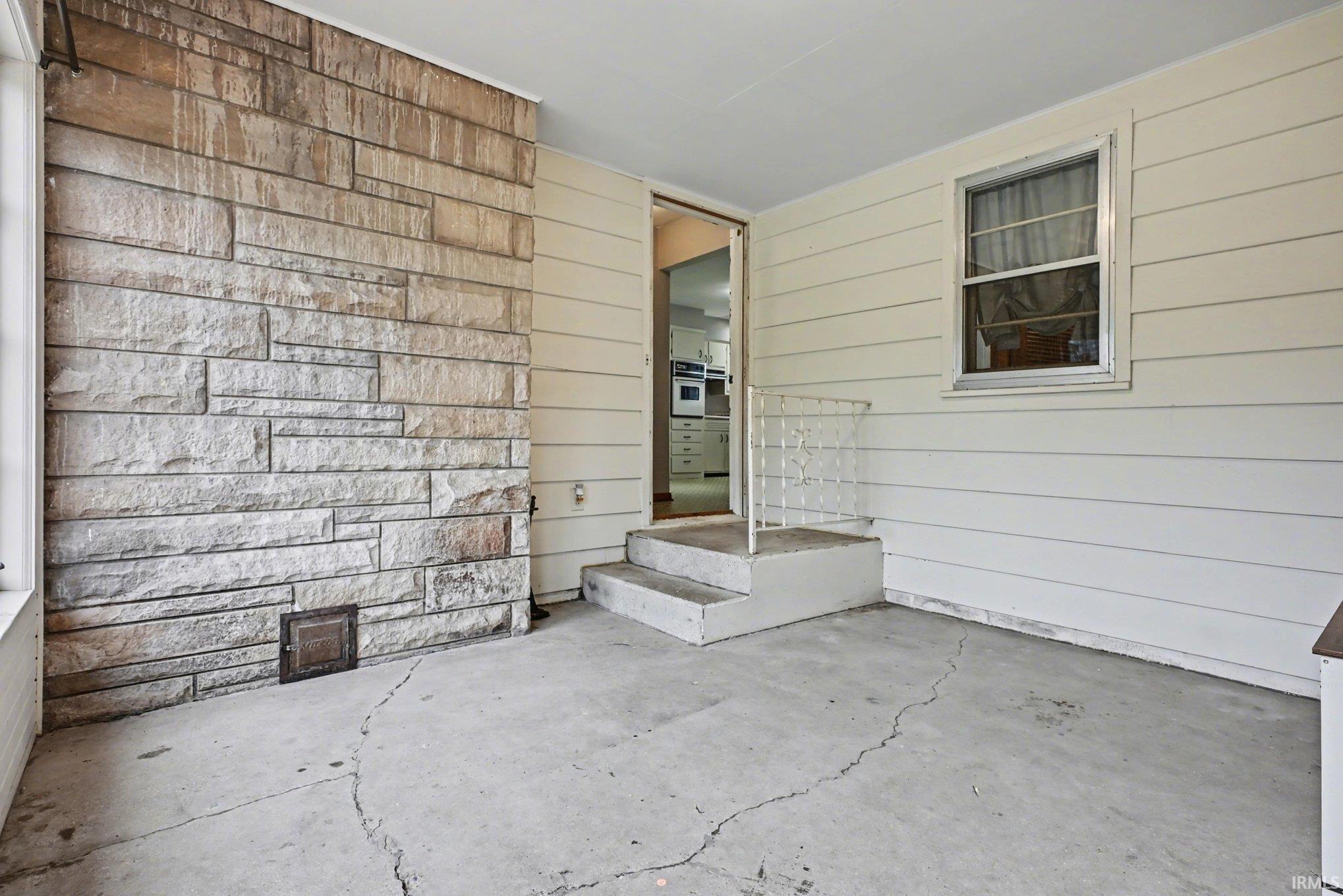 Covered patio space featuring a stone accent wall, concrete flooring, and white horizontal siding