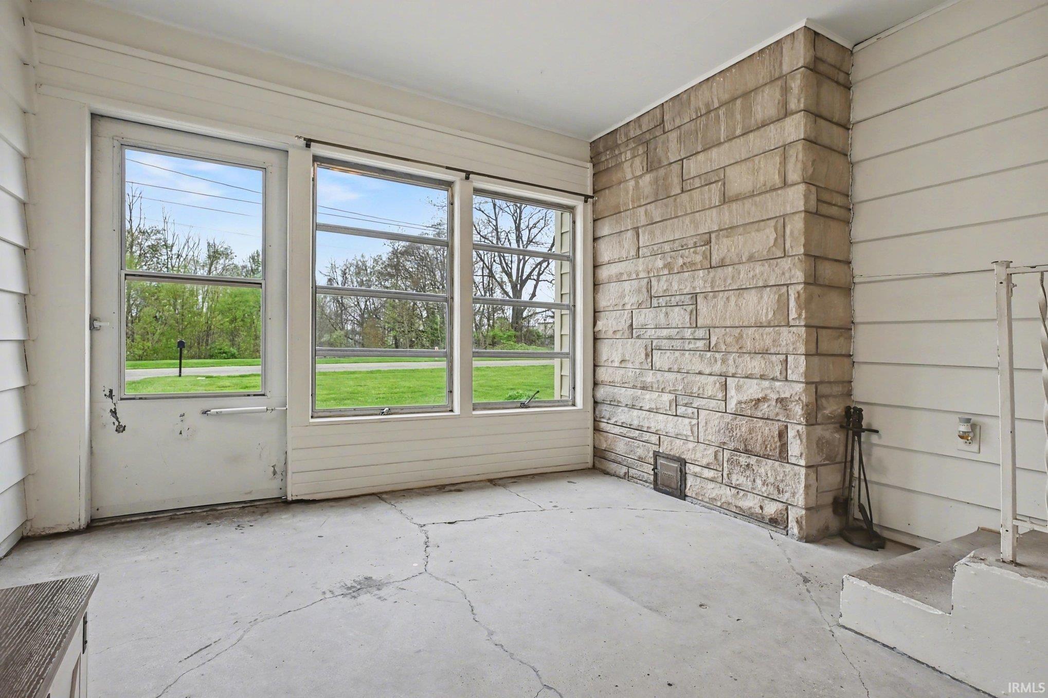 Enclosed sunroom featuring a stone accent wall, multiple large windows, a full-light exterior door, and a concrete floor