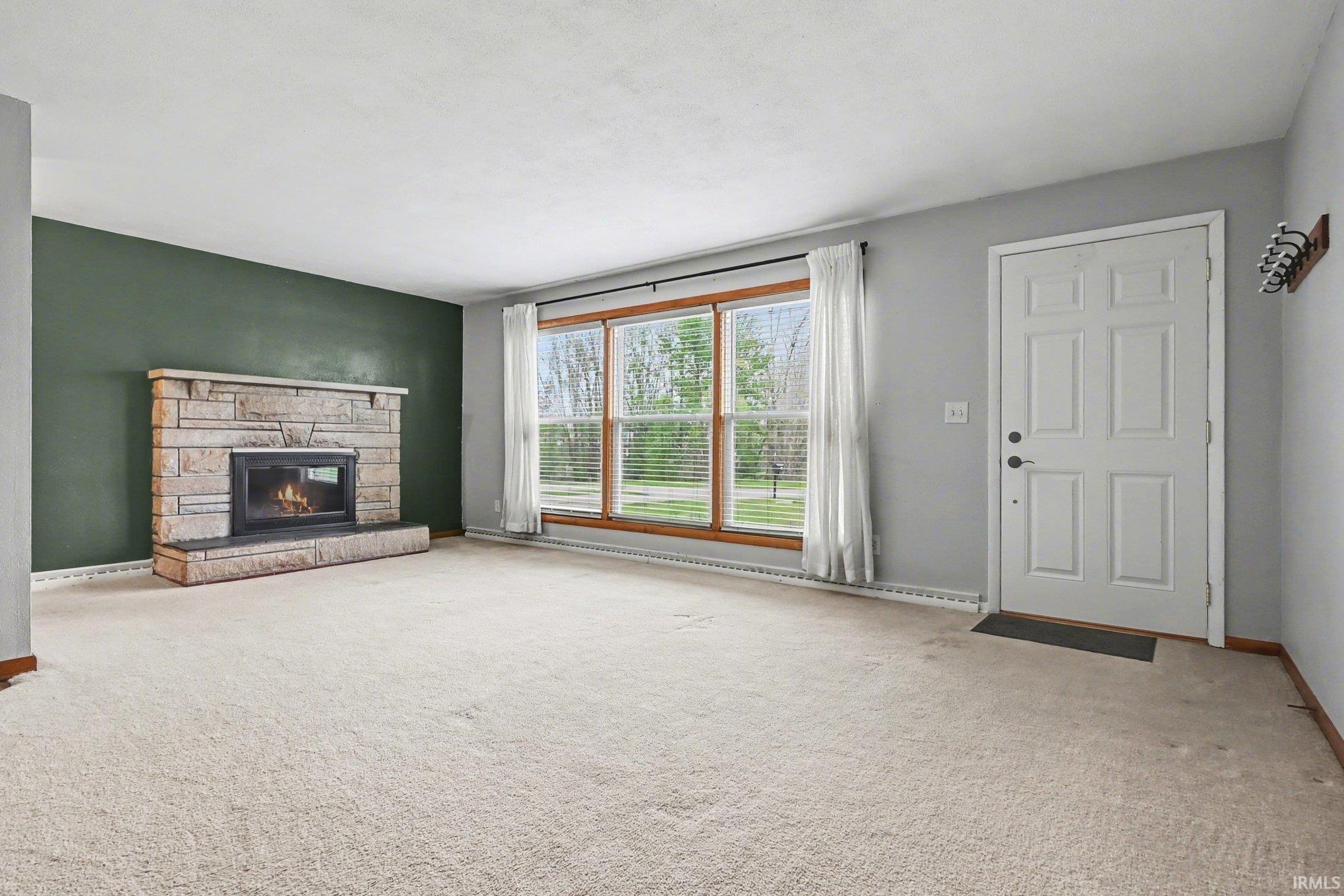 Inviting living space featuring a stone fireplace with hearth, a multi-pane window with wood trim, and light-toned carpeting