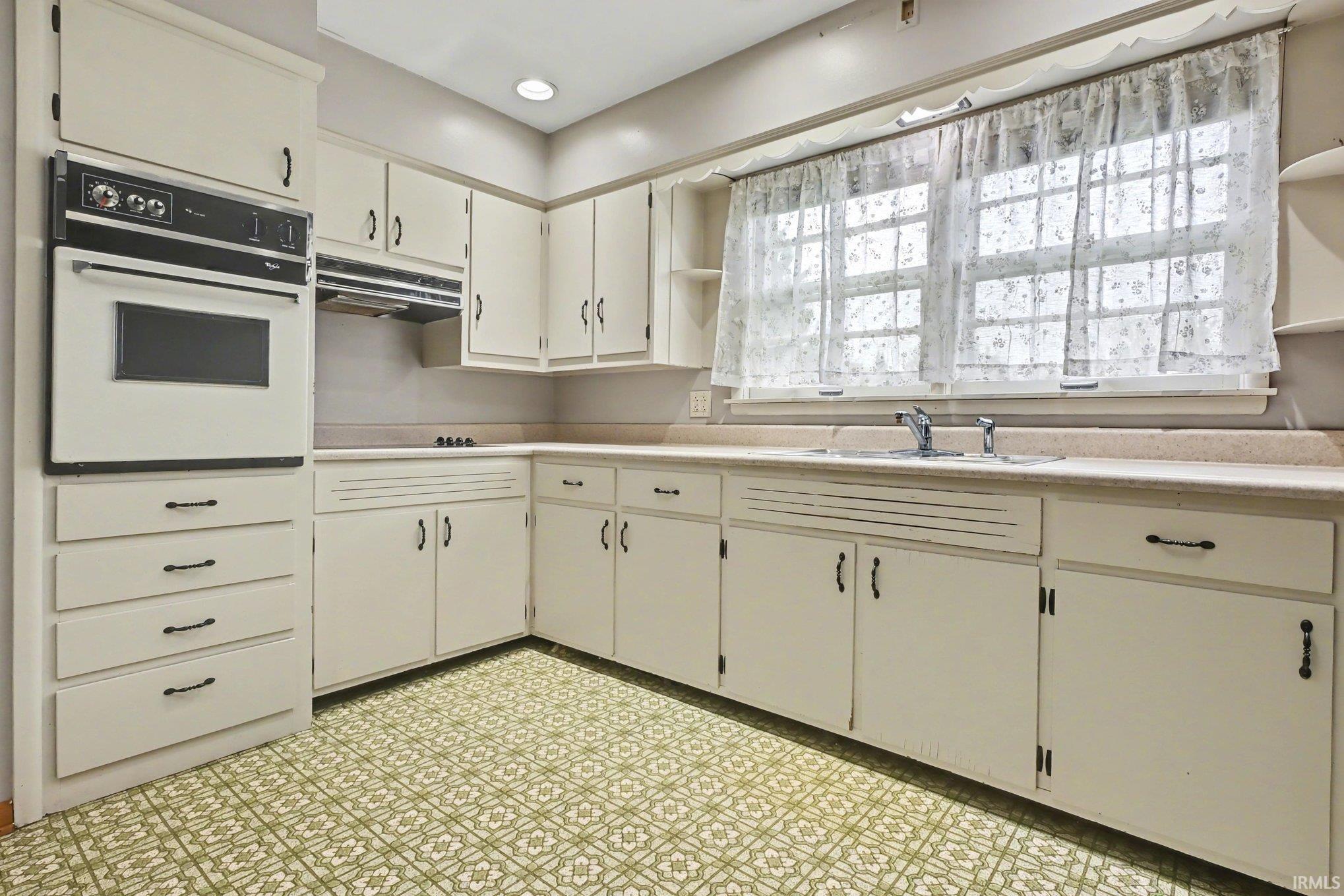 Kitchen with built-in wall oven, white cabinetry, integrated sink, light-colored countertops, and patterned floor tile