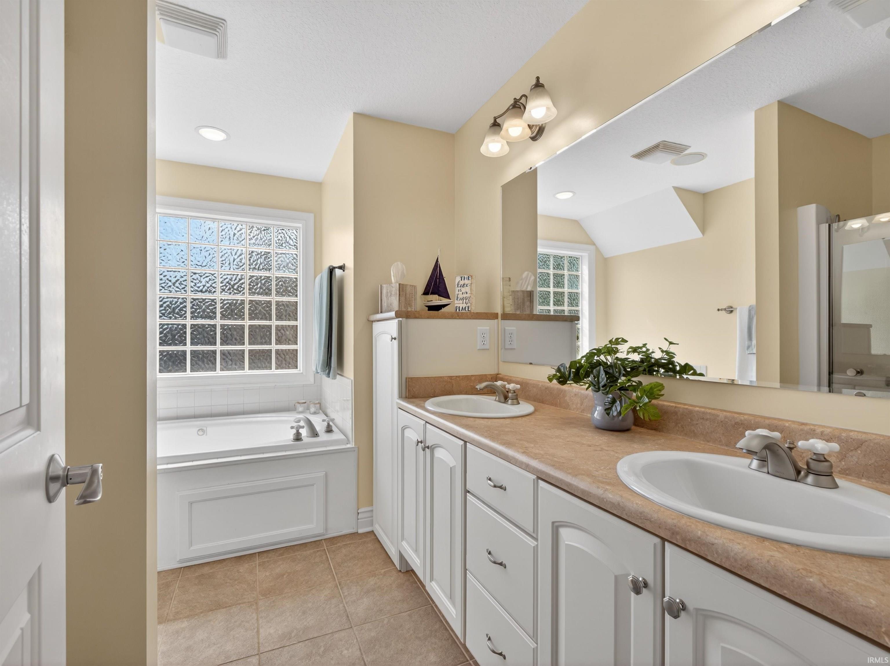 Full bathroom featuring a garden tub, double vanity, light tile patterned floors, and recessed lighting