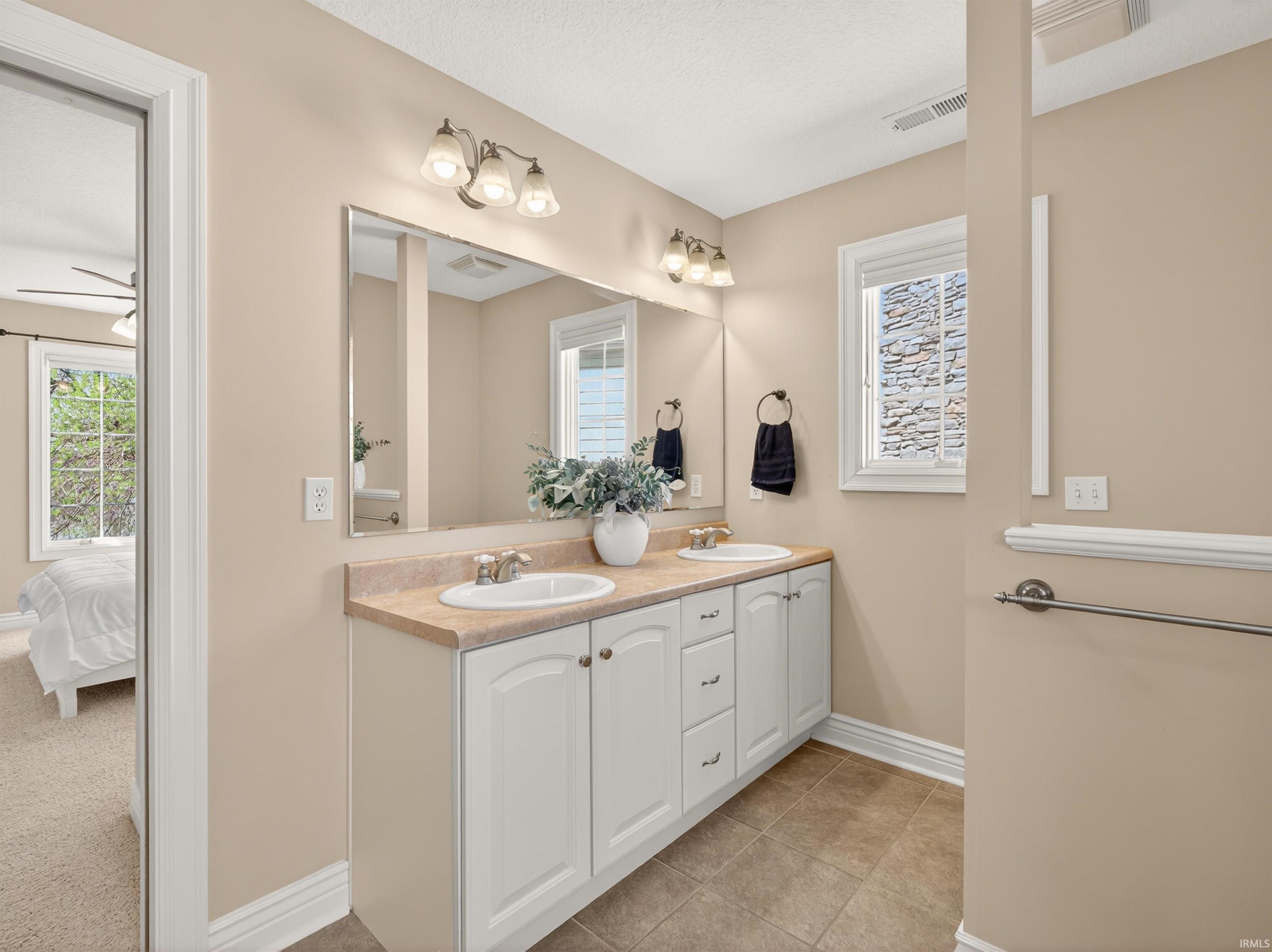 Ensuite bathroom featuring double vanity, light tile patterned flooring, and a ceiling fan