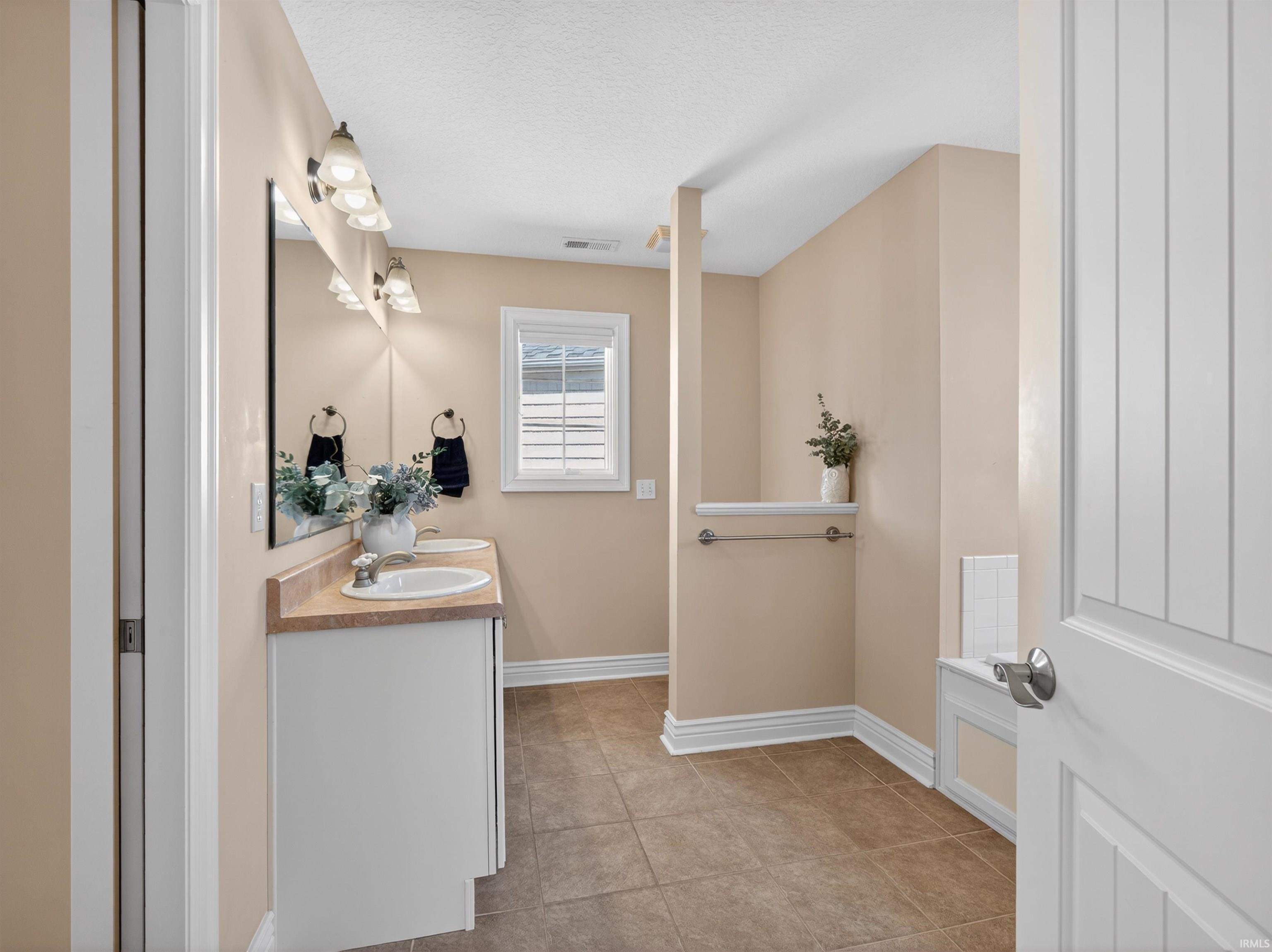 Full bathroom with double vanity, light tile patterned floors, a textured ceiling, and a bath