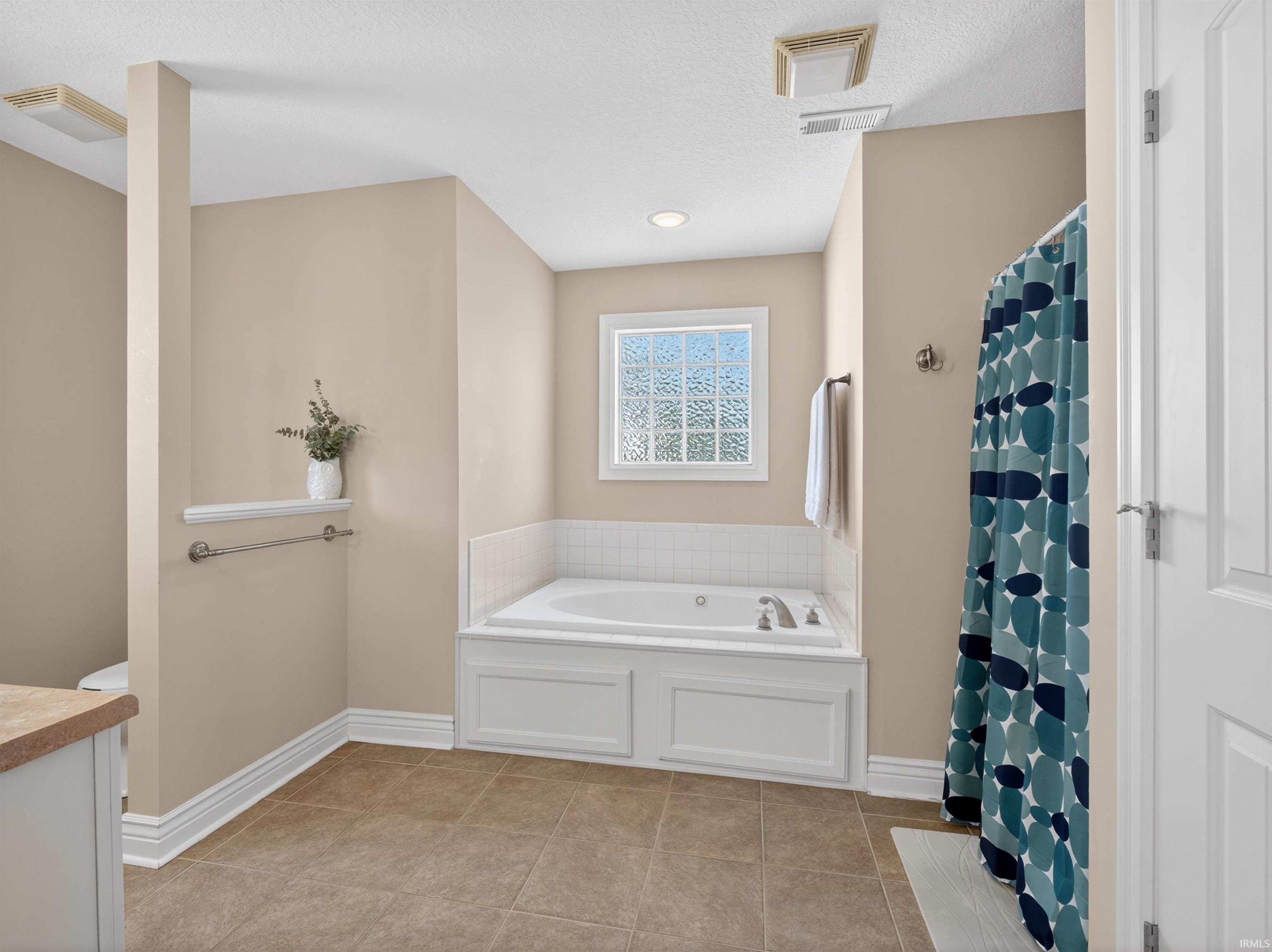 Bathroom with curtained shower, vanity, light tile patterned flooring, and a garden tub