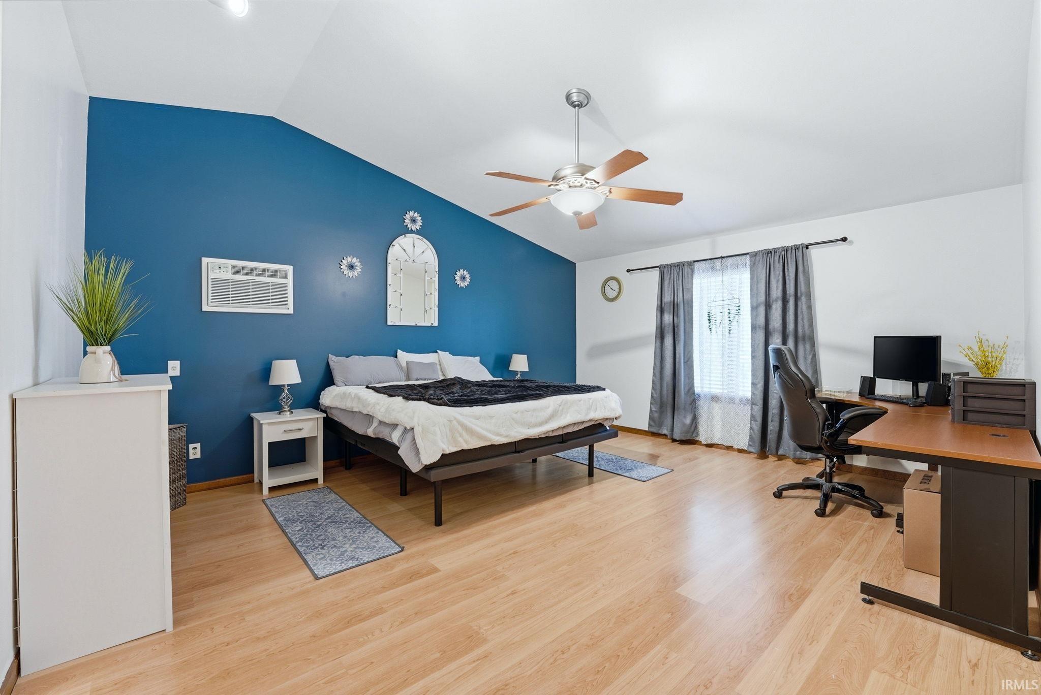 Spacious room featuring vaulted ceilings, wood-finish flooring, and a ceiling fan with integrated lighting