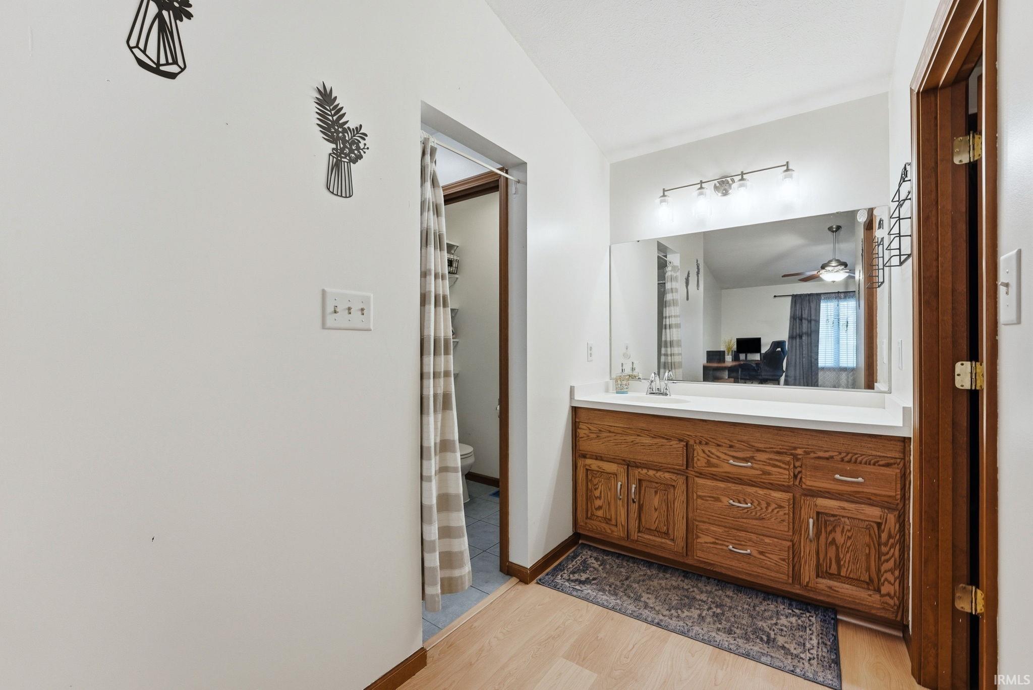Bathroom featuring a wood-finish vanity with multiple storage drawers and cabinet doors, a spacious countertop, a large wall-mounted mirror, and a four-bulb vanity light fixture