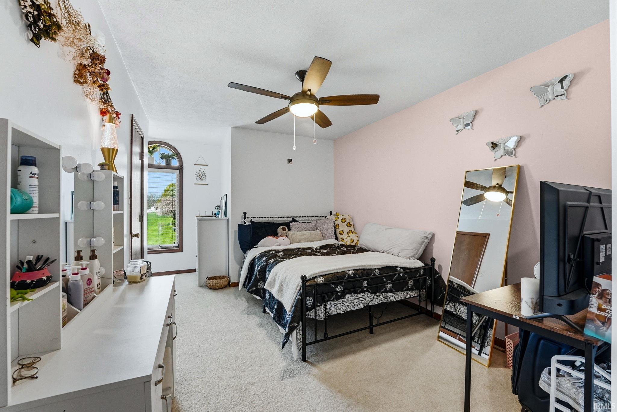 Carpeted room featuring a ceiling fan with integrated lighting, a rounded arch window with wood-finish trim, and a white built-in vanity with shelving