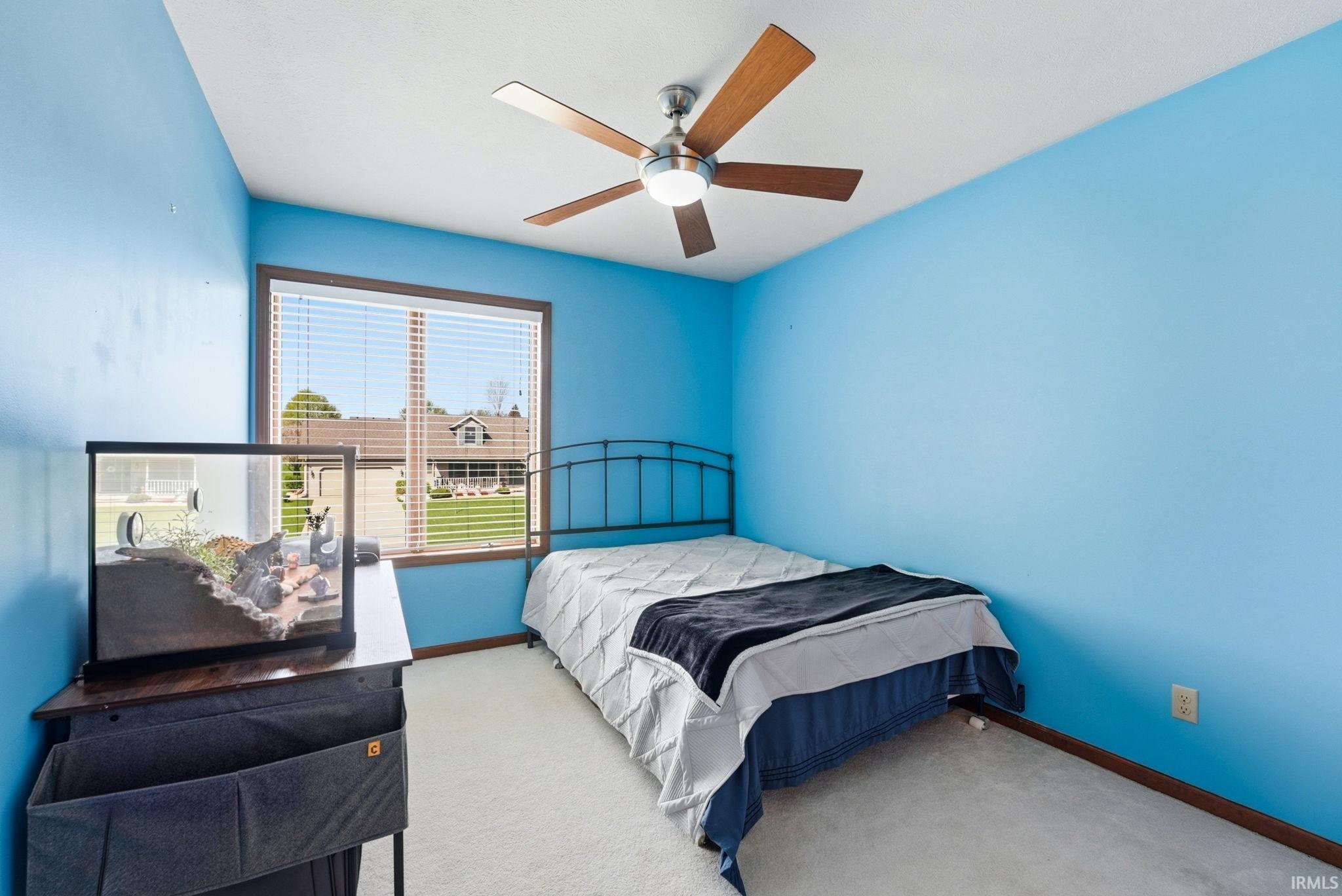 Room featuring a large window with blinds, a ceiling fan with wood-finish blades, and neutral carpet flooring