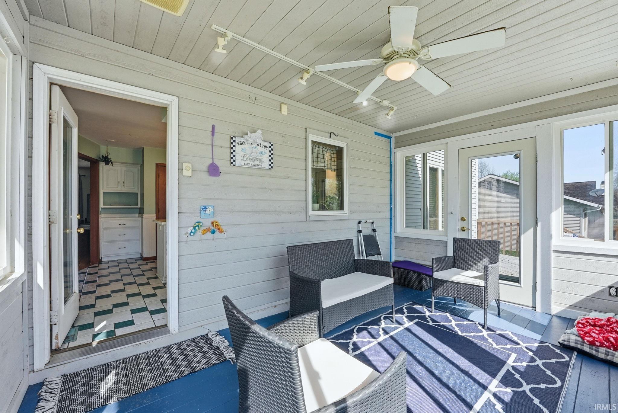 Enclosed porch featuring a ceiling fan with integrated lighting, wood-paneled walls, and blue-painted flooring