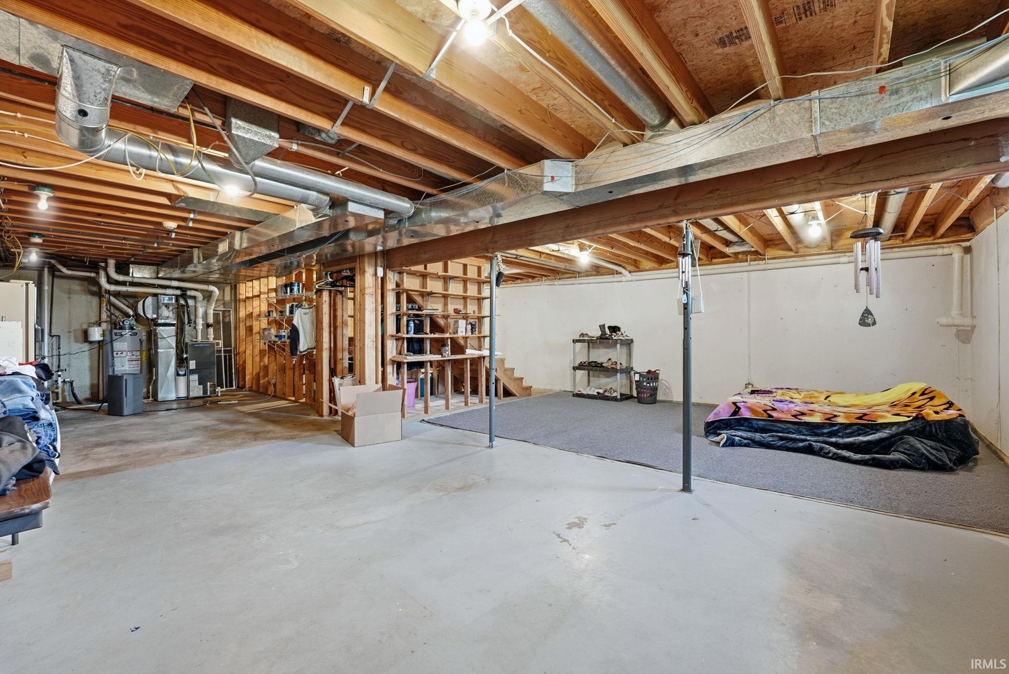 Unfinished basement featuring exposed wood joists, concrete flooring, and a carpeted area