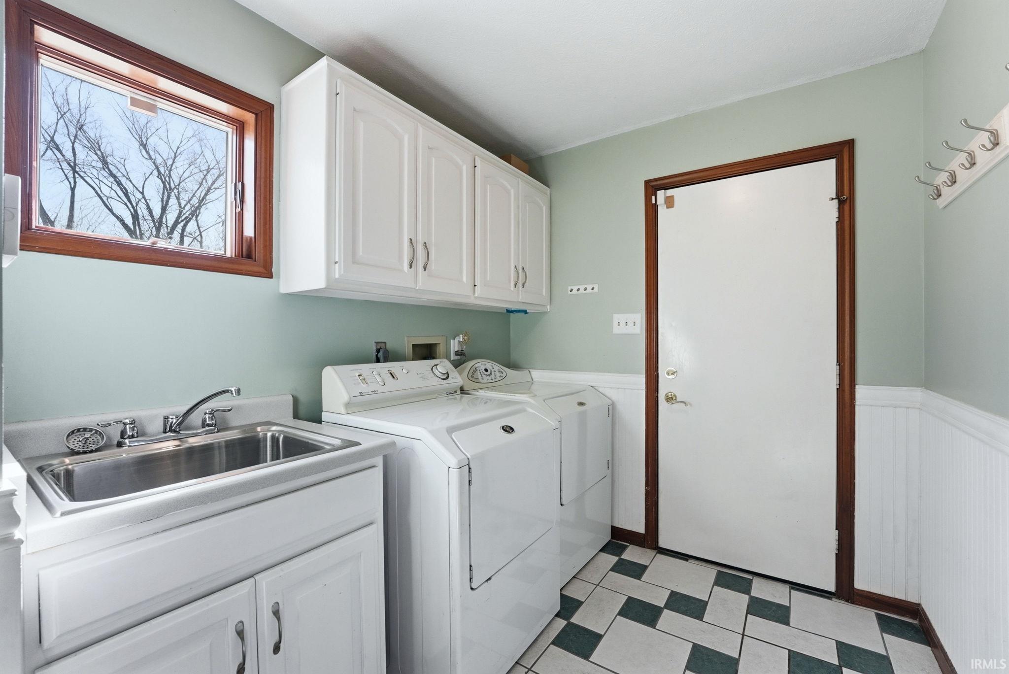 Utility room featuring a stainless steel sink with a chrome faucet, white cabinetry, a wood-framed window, and a patterned floor