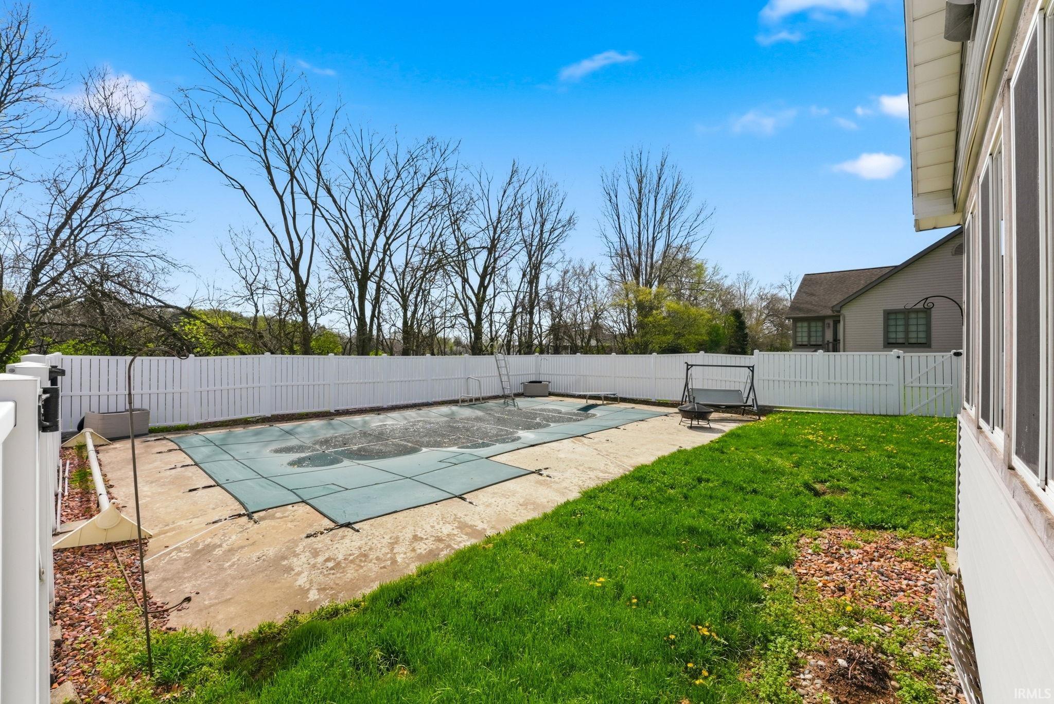Fenced backyard featuring an in-ground pool with a safety cover, concrete patio, and manicured lawn