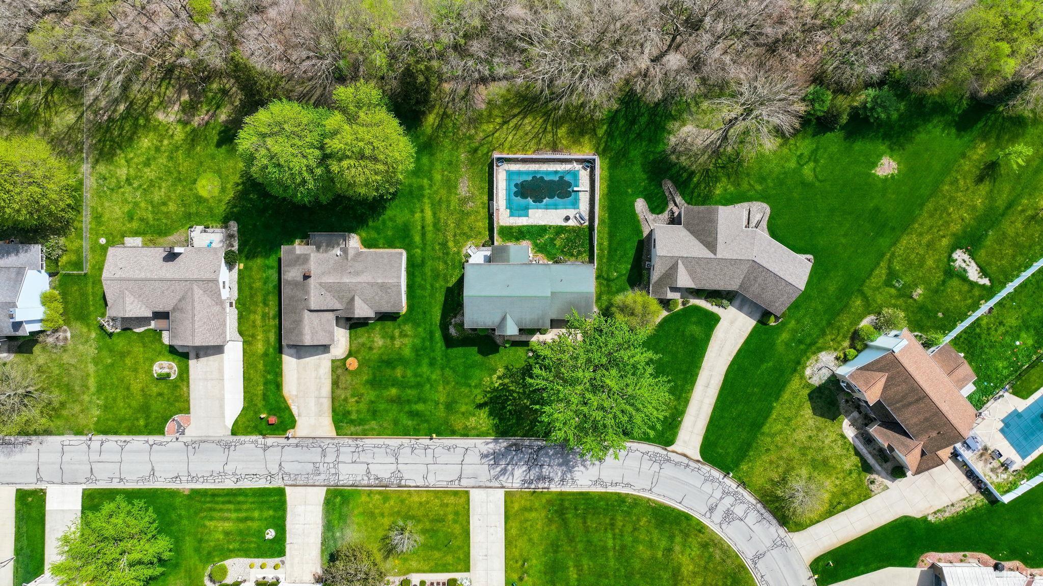 Neighborhood aerial showcasing multiple properties, lush green lawns, and mature trees
