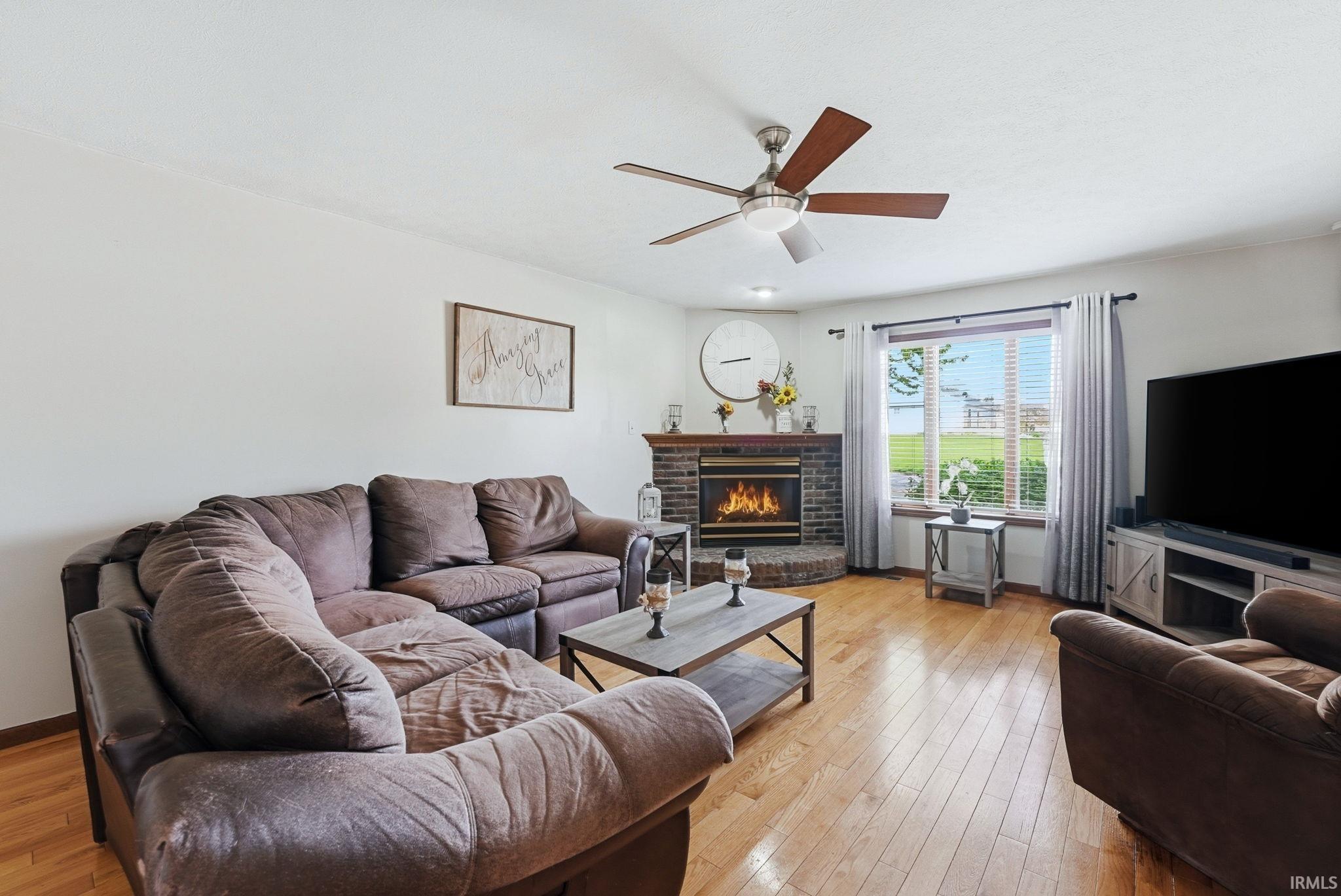 Living area with wood-finish flooring, a corner brick fireplace, and a ceiling fan