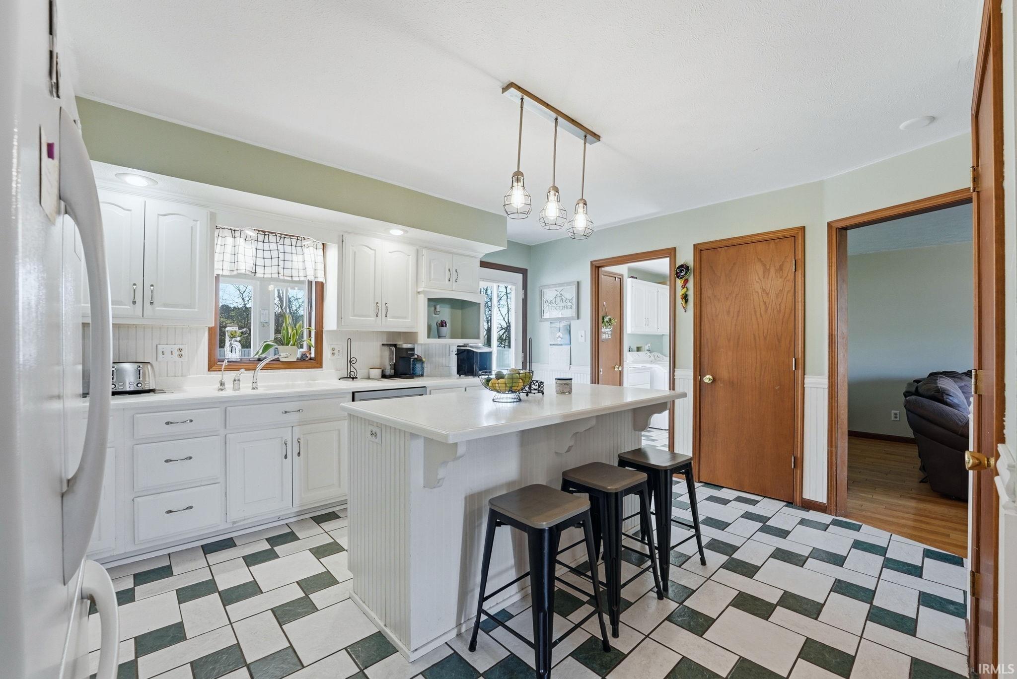 Spacious kitchen featuring white cabinetry, a center island with pendant lighting, a white tile backsplash, and patterned floor tiles
