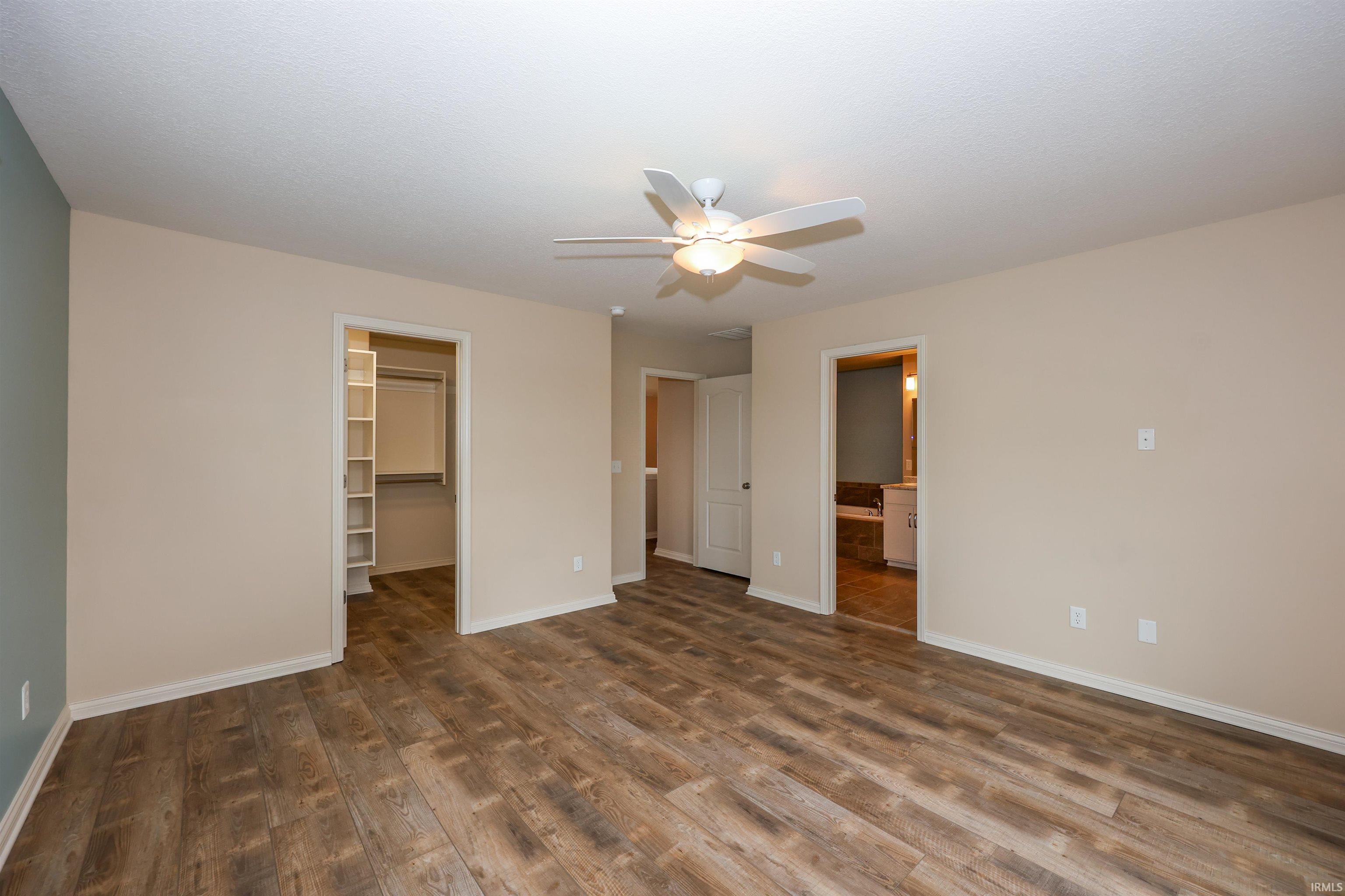 Spacious interior room with wood-finish flooring, neutral wall tones, and a ceiling fan with integrated lighting