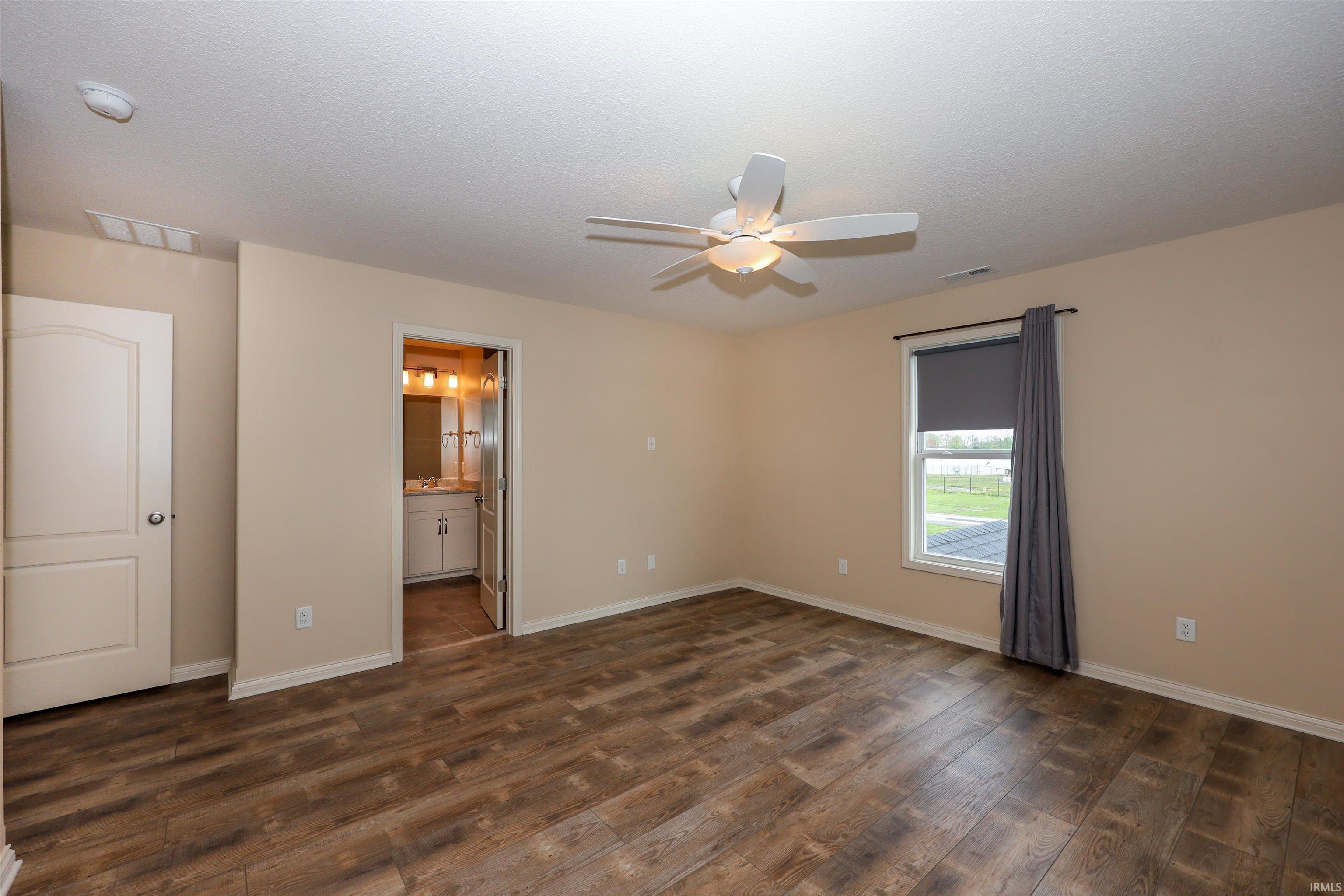 Spacious room featuring wood-finish flooring, a ceiling fan with light fixture, and a window with roller shade