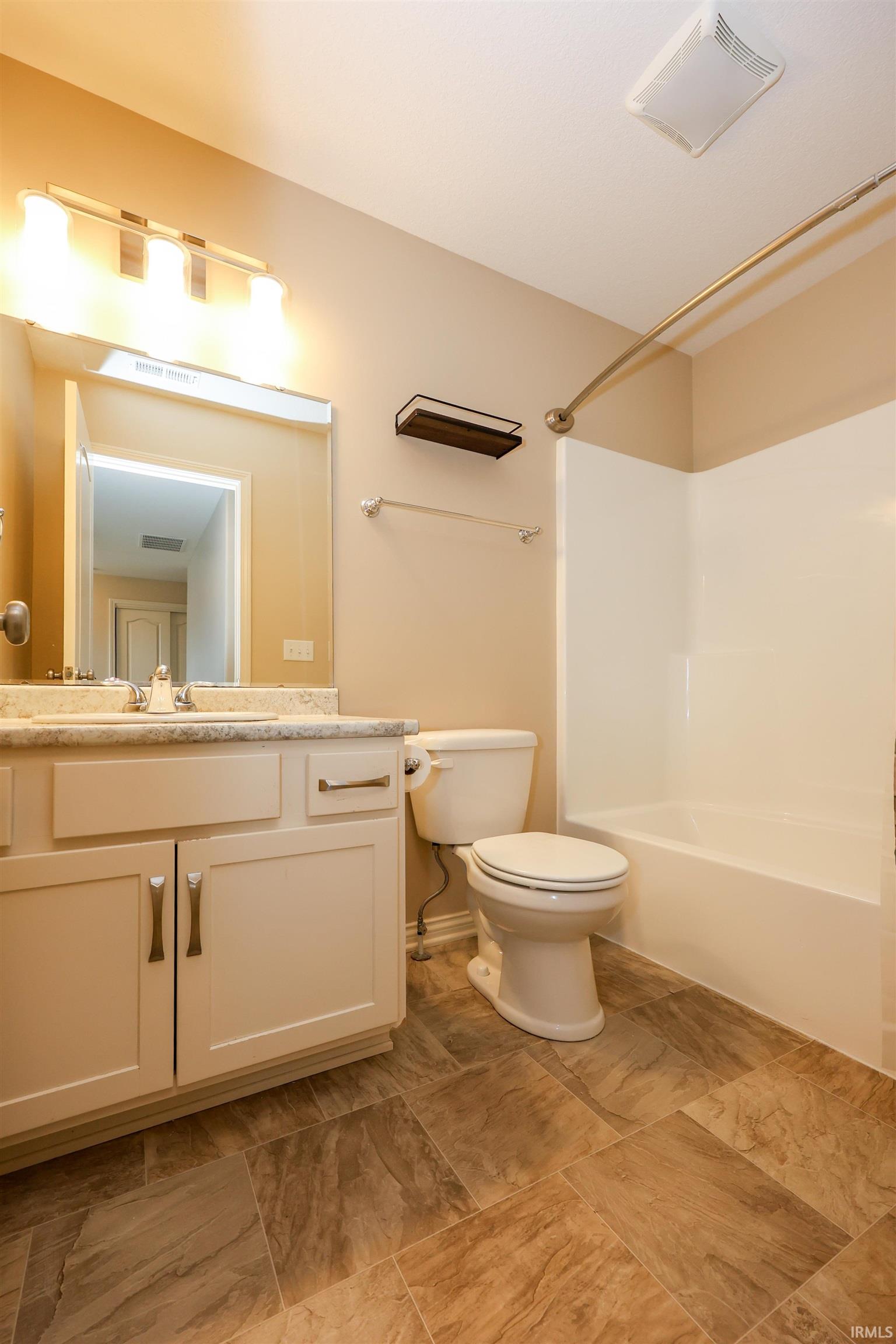 Bathroom featuring white vanity cabinetry with brushed nickel hardware, light-toned countertop, a shower/tub combination with a curved rod, and large format tile flooring