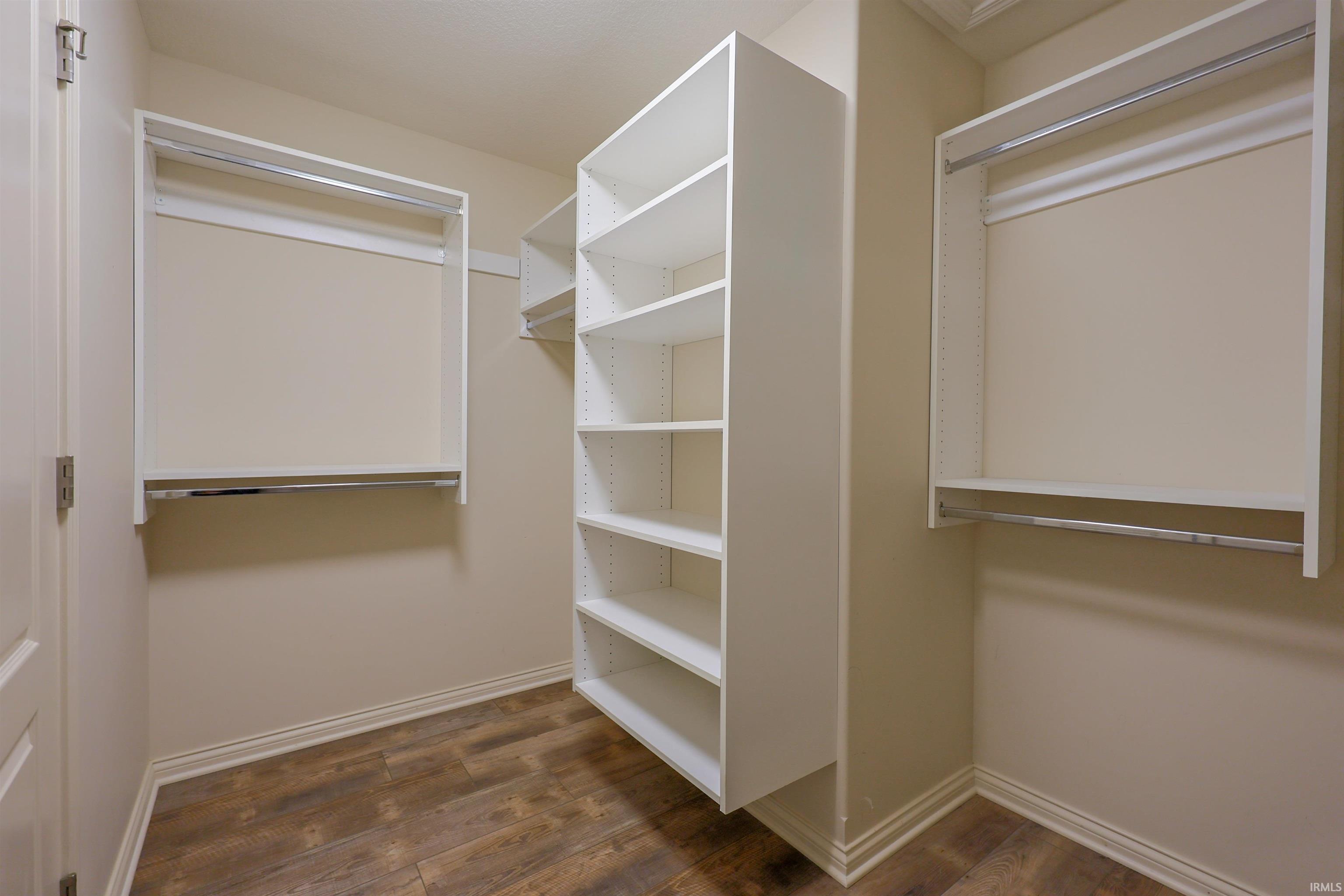 Walk-in closet featuring built-in shelving, dual hanging rods, and wood-finish flooring