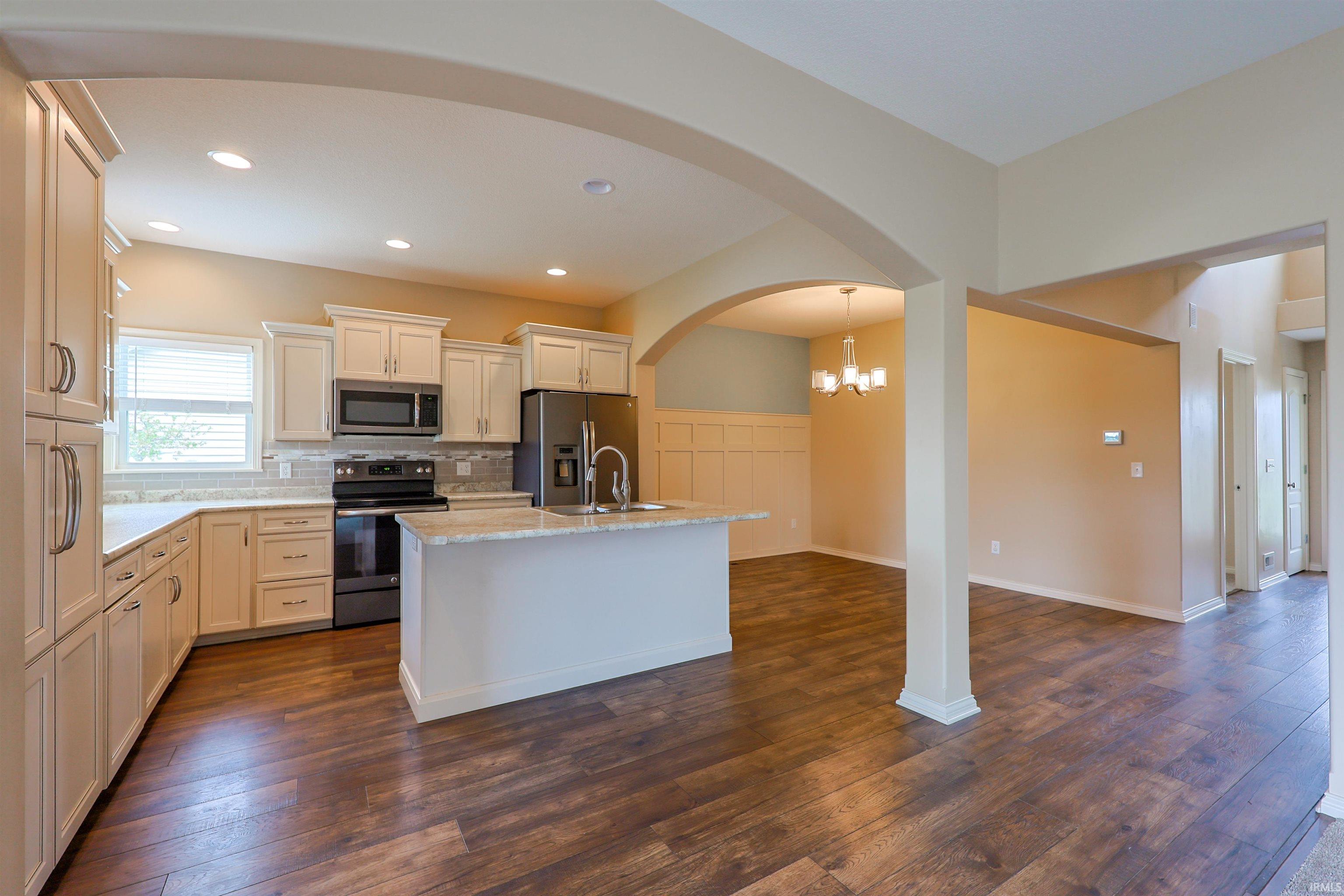 Kitchen featuring wood-finish flooring, white cabinetry, stainless steel appliances, and a central island with a sink