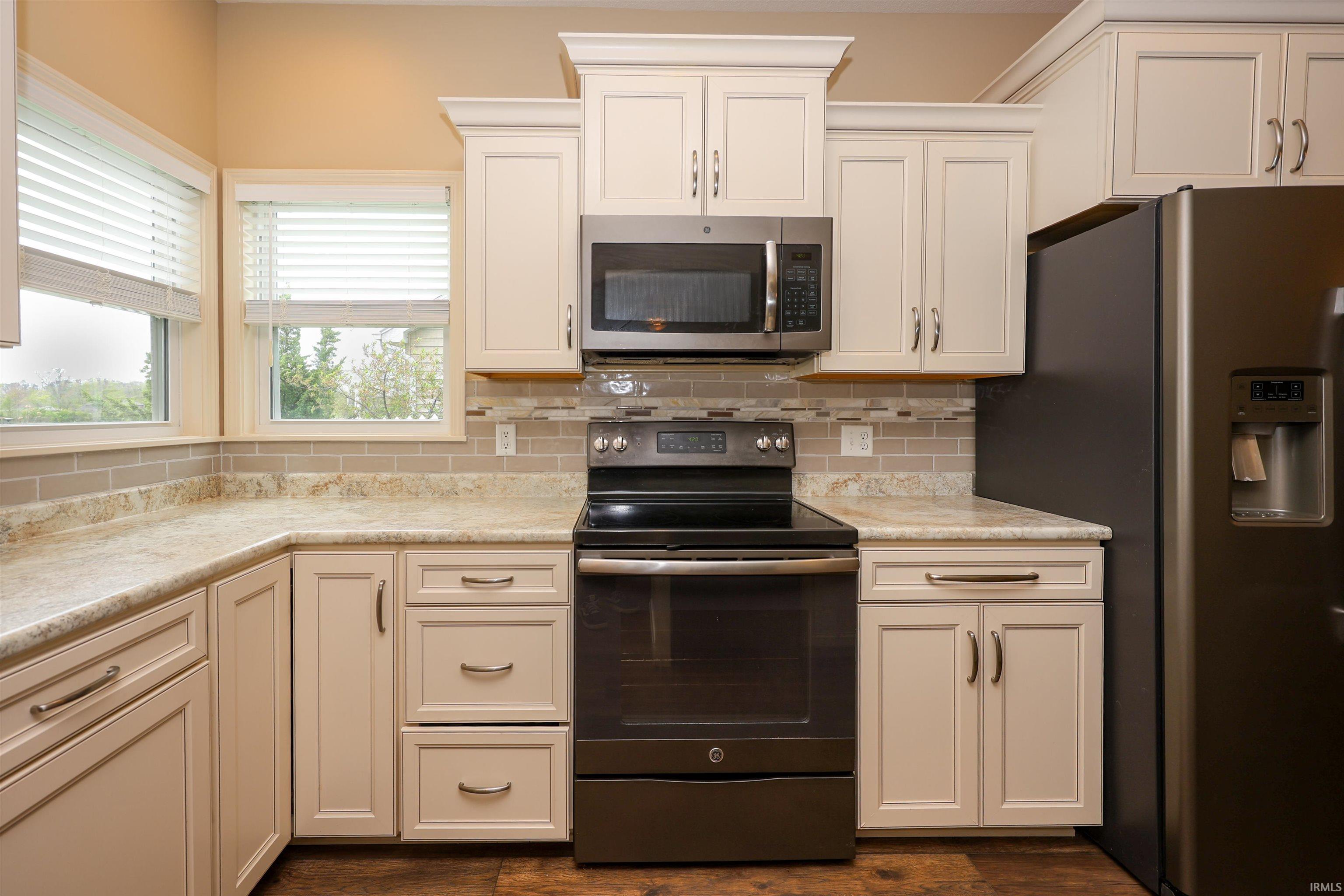 Kitchen featuring a built-in microwave, an electric range, stainless steel refrigerator, light-toned cabinetry, and a tile backsplash
