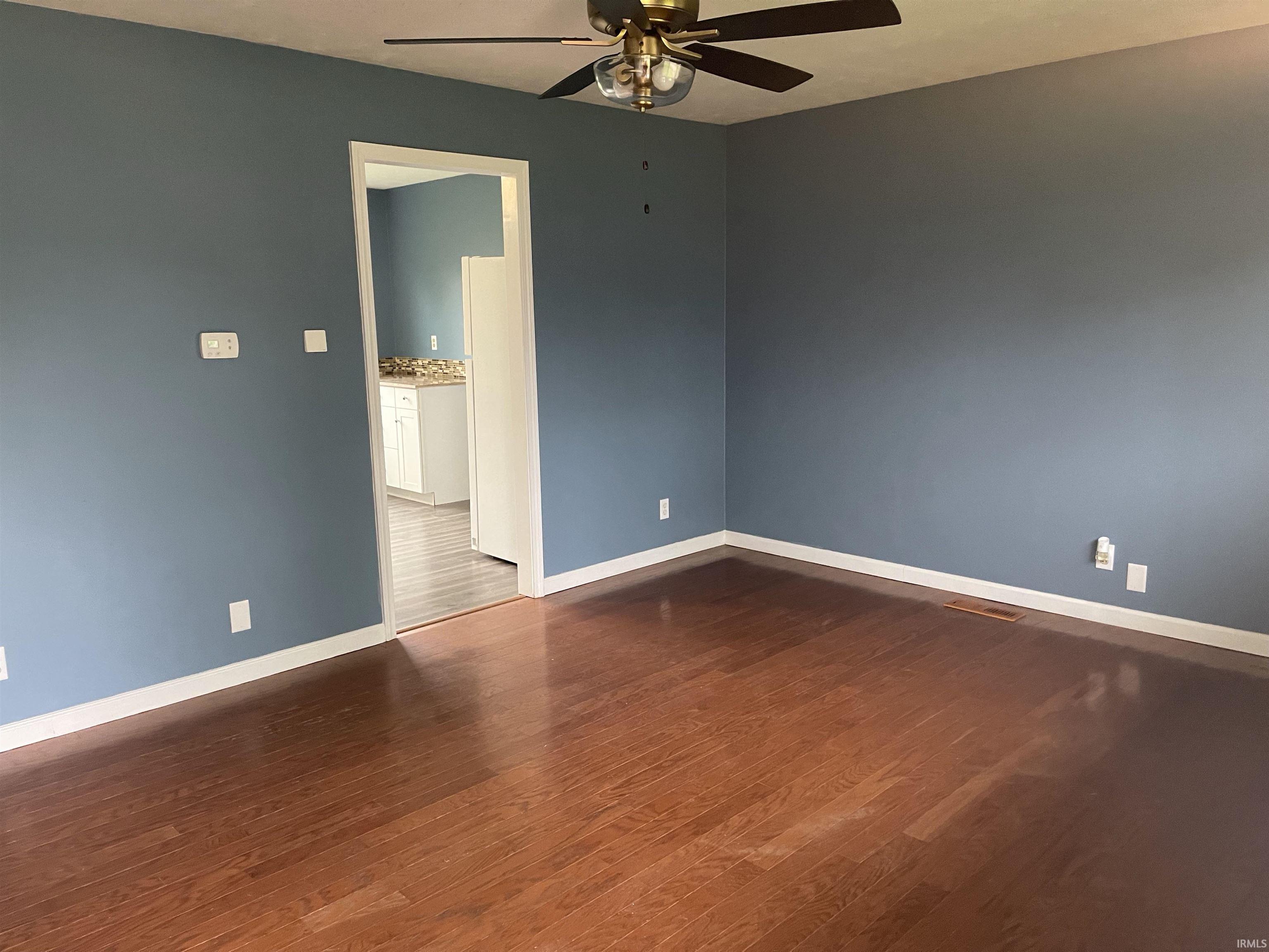 Spacious interior room featuring rich wood-finish flooring, blue-painted walls, and bright white trim