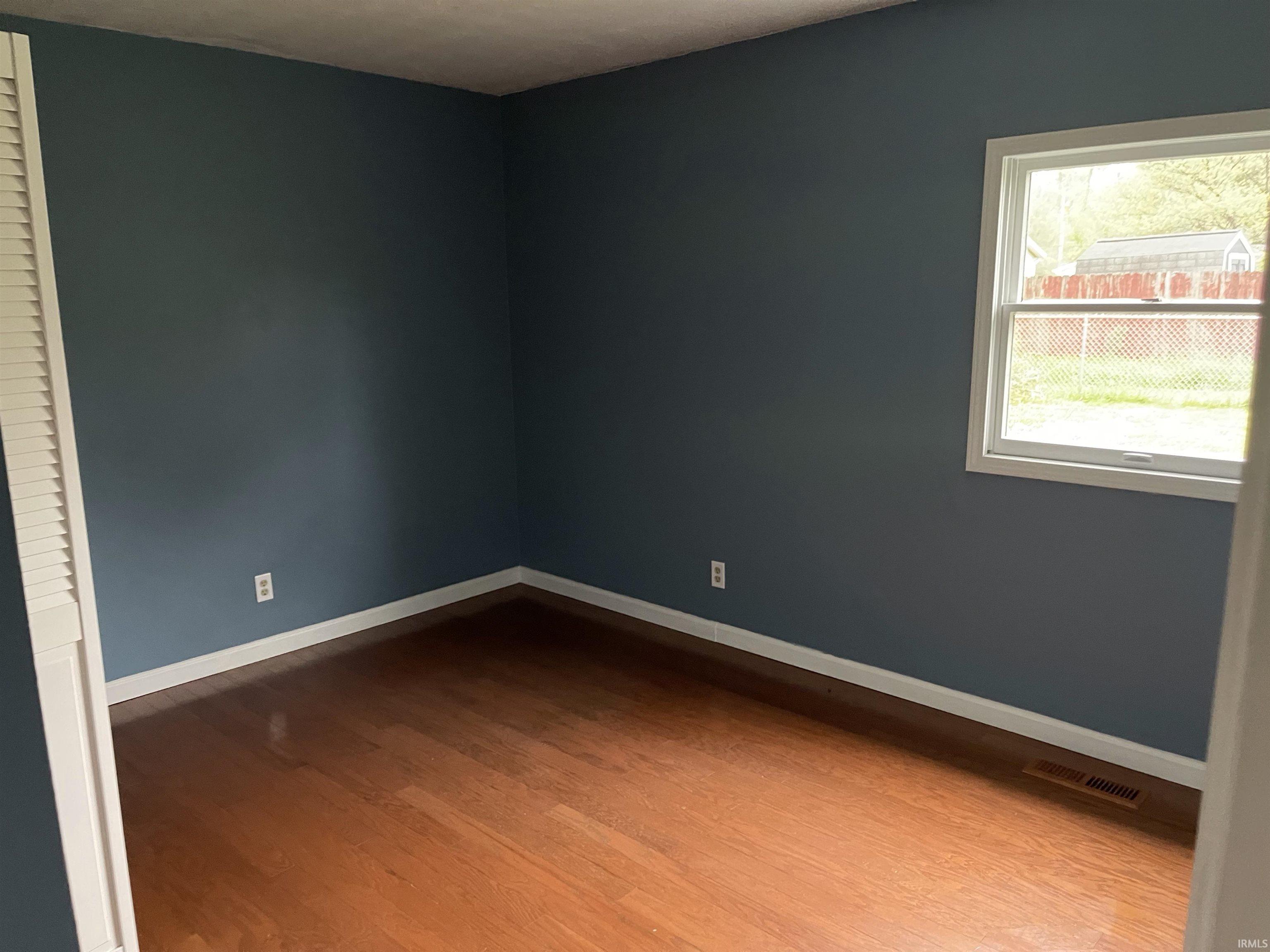 Interior room featuring wood-finish flooring, blue-painted walls, white baseboards, and a single window with white trim