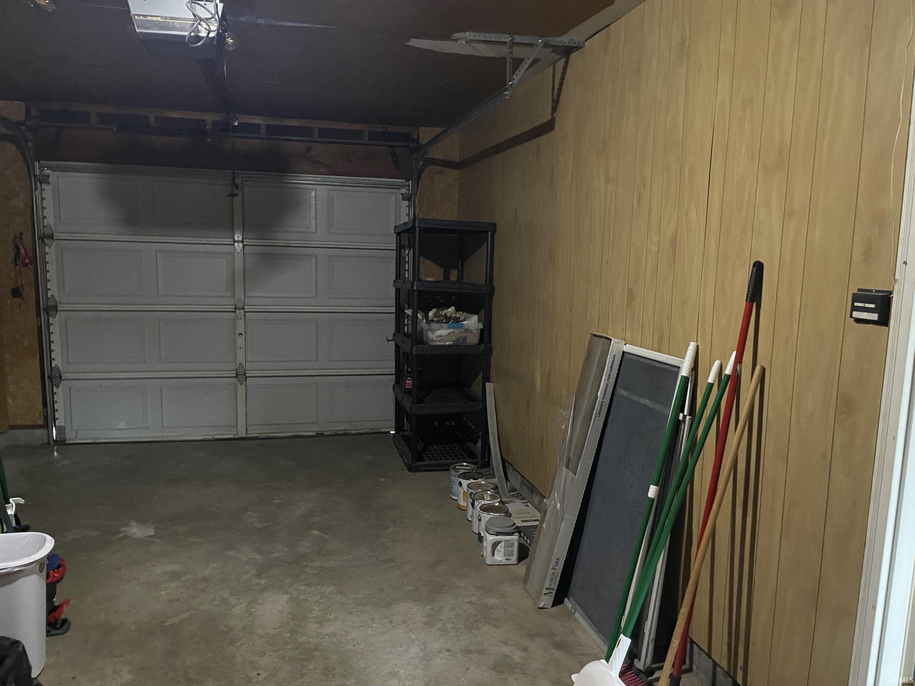 Attached garage featuring a panel garage door, concrete flooring, and light-toned wood paneling on the side wall