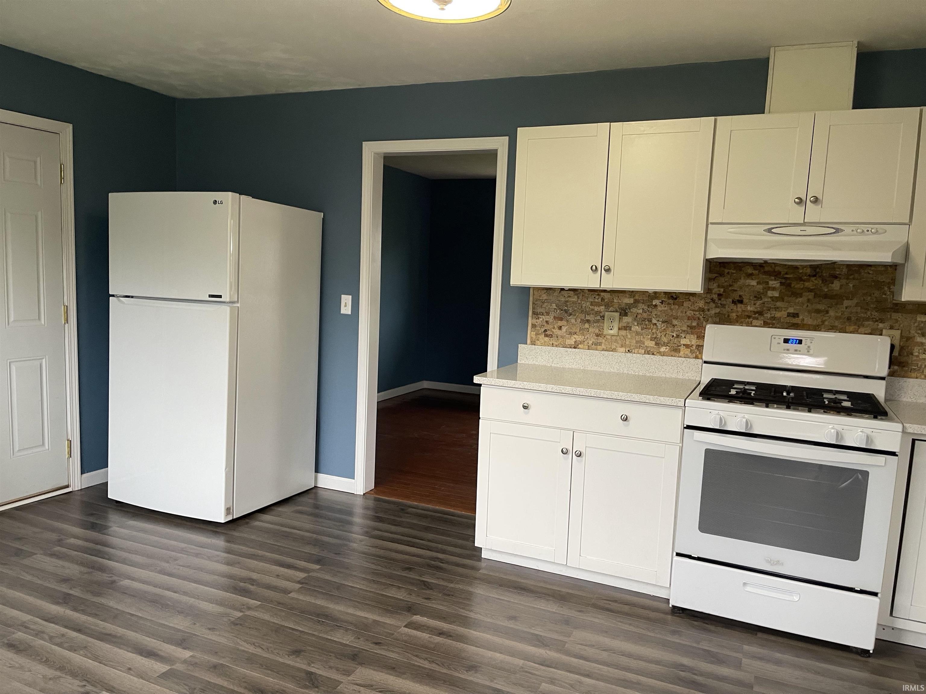 Kitchen featuring wood-finish flooring, white cabinetry, a stone-look backsplash, light-toned countertops, and a white gas range