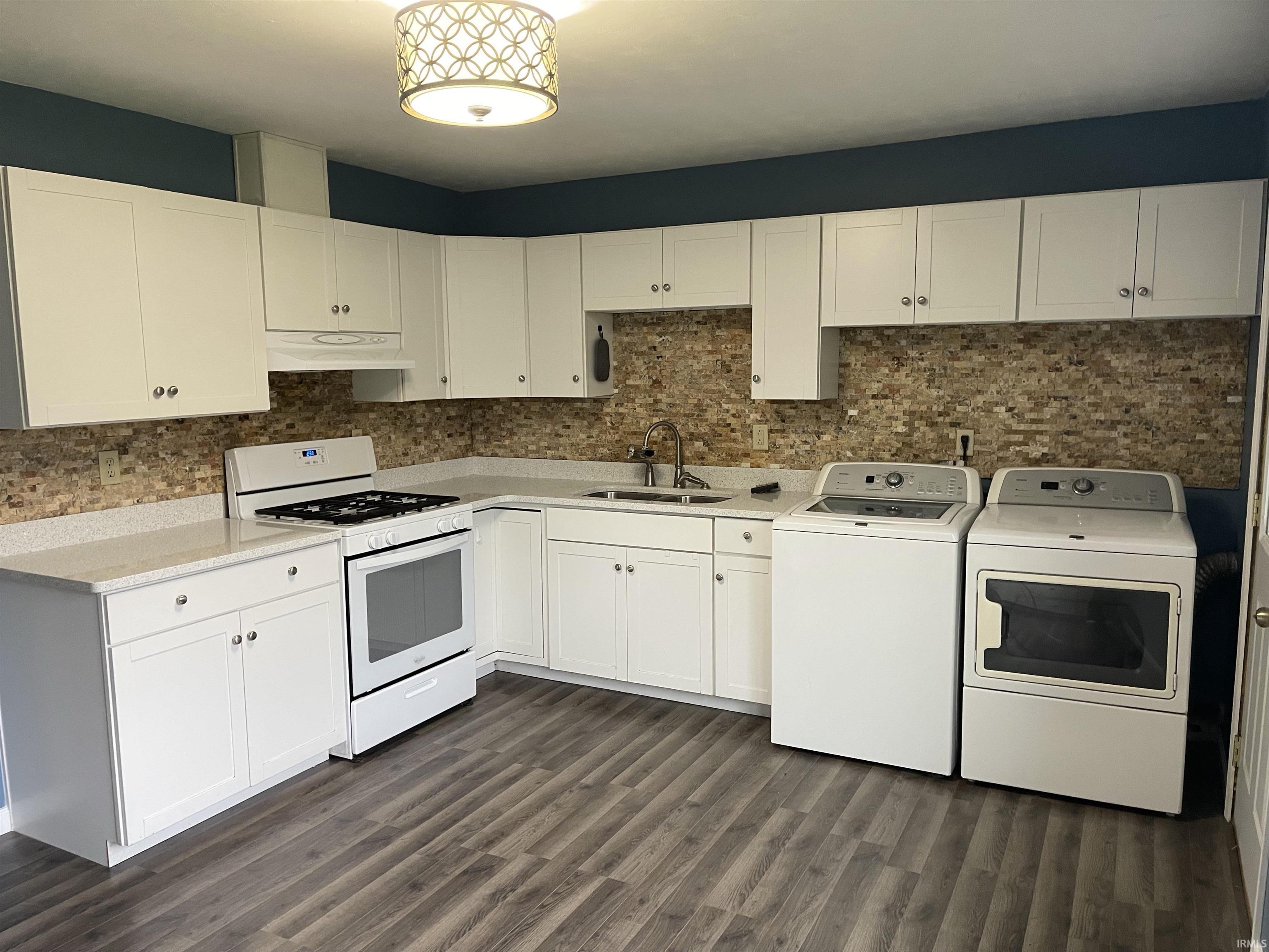 Kitchen featuring white cabinetry with brushed nickel hardware, light-toned countertops, stone mosaic backsplash, and wood-finish flooring