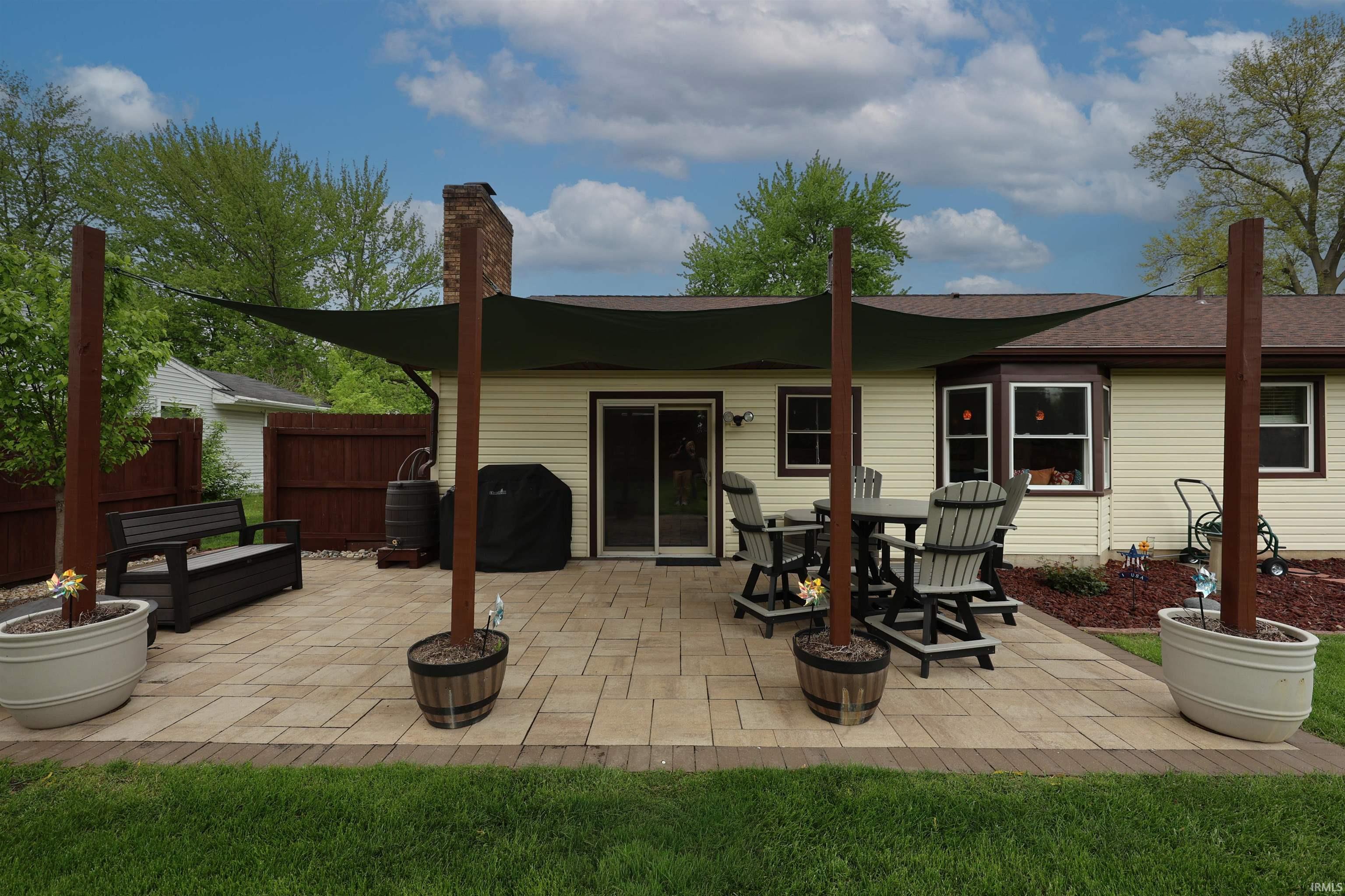 Spacious paver patio with a shade sail structure, featuring a sliding glass door entry to the interior, a bay window, and exterior siding