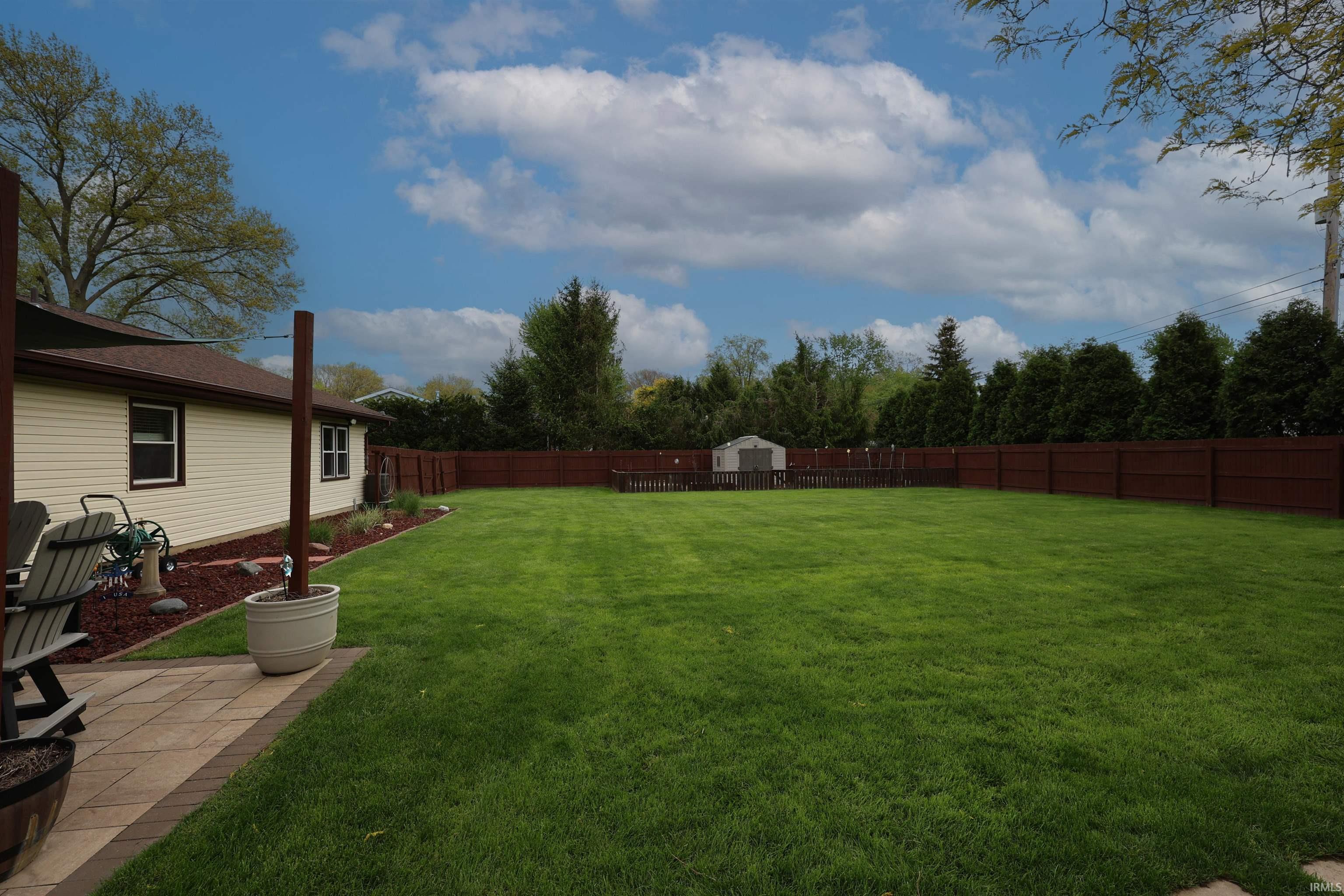 Expansive backyard featuring a lush lawn, privacy fencing, a storage shed, and a paver patio