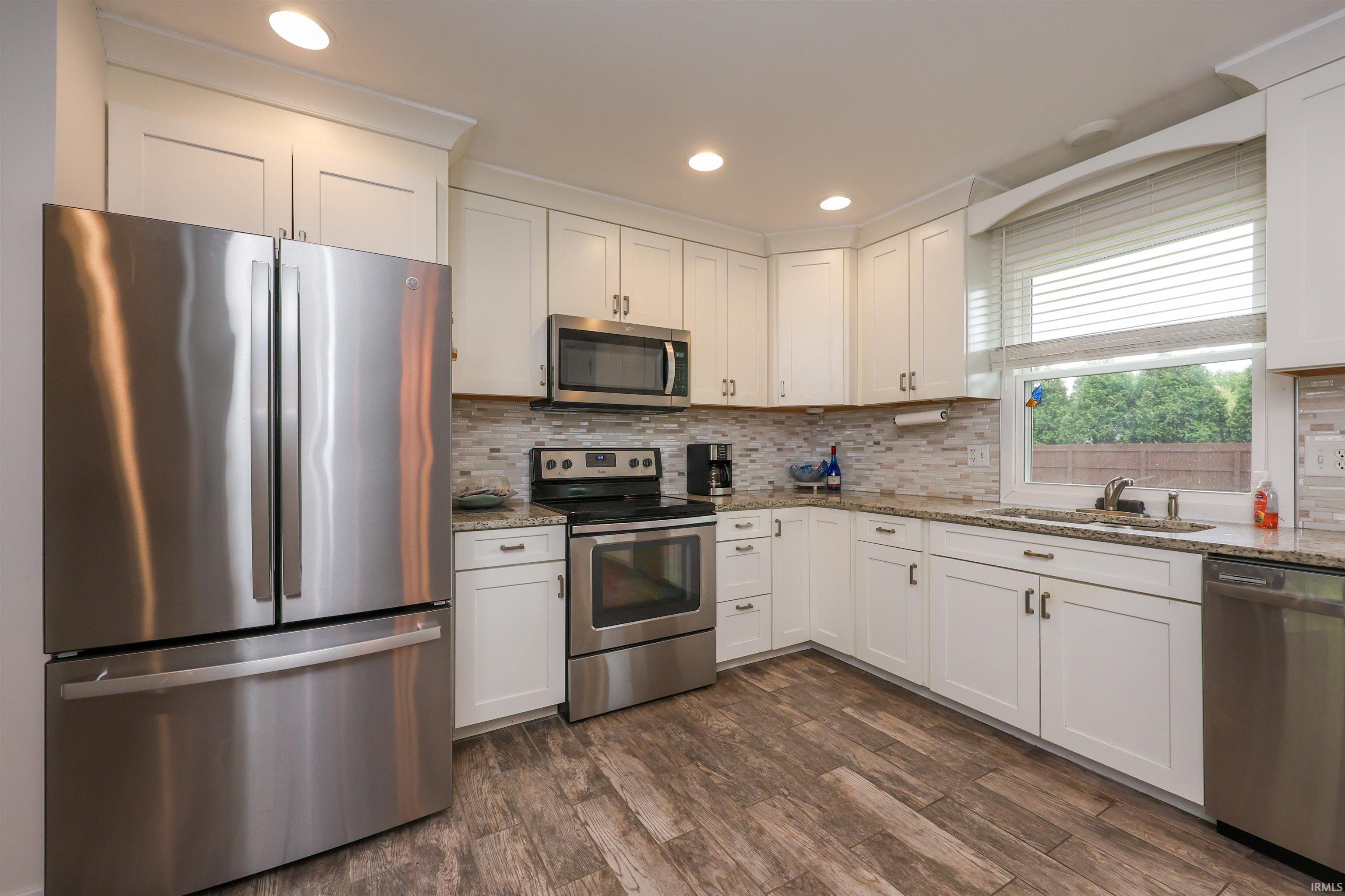 Kitchen featuring white shaker cabinetry, stainless steel appliances, speckled countertops, a mosaic tile backsplash, and wood-finish flooring