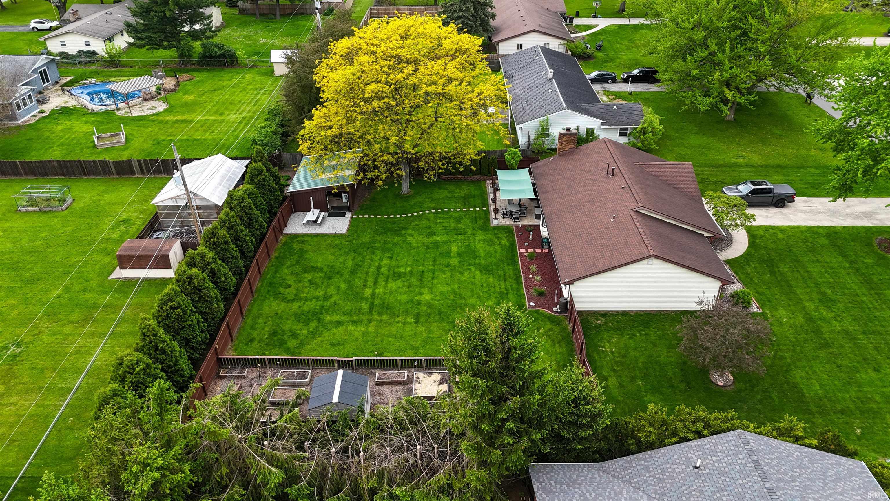 Spacious private backyard featuring a manicured lawn, established perimeter fencing, mature trees, and a built-in patio area